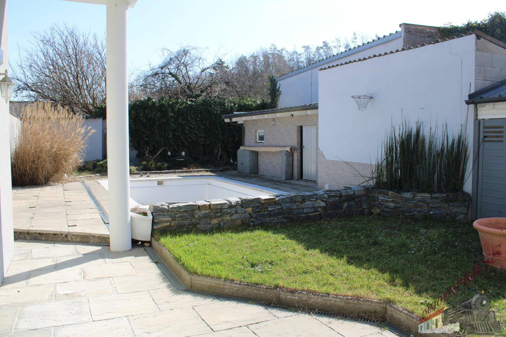 Gartenbereich mit gepflasterter Terrasse, Rasenfläche und einem kleinen Pool.
