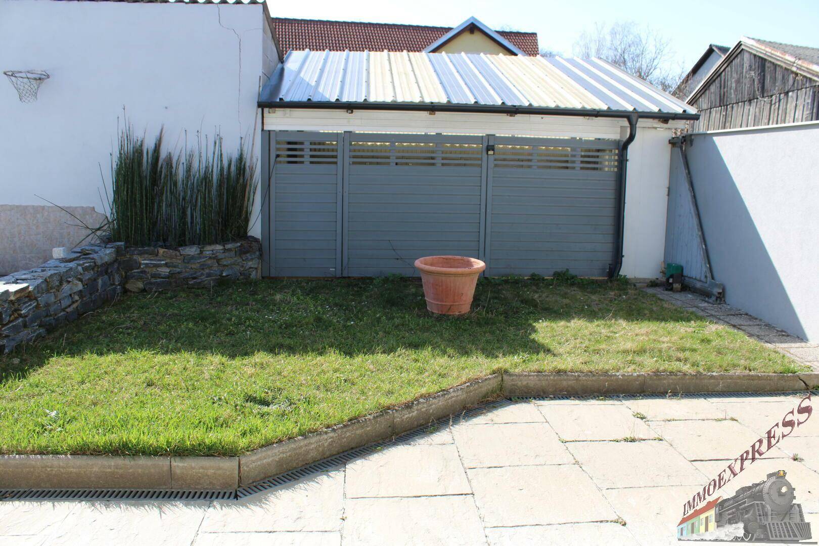 Kleiner Gartenbereich mit Rasen, Pflastersteinen und einem Holzschuppen.