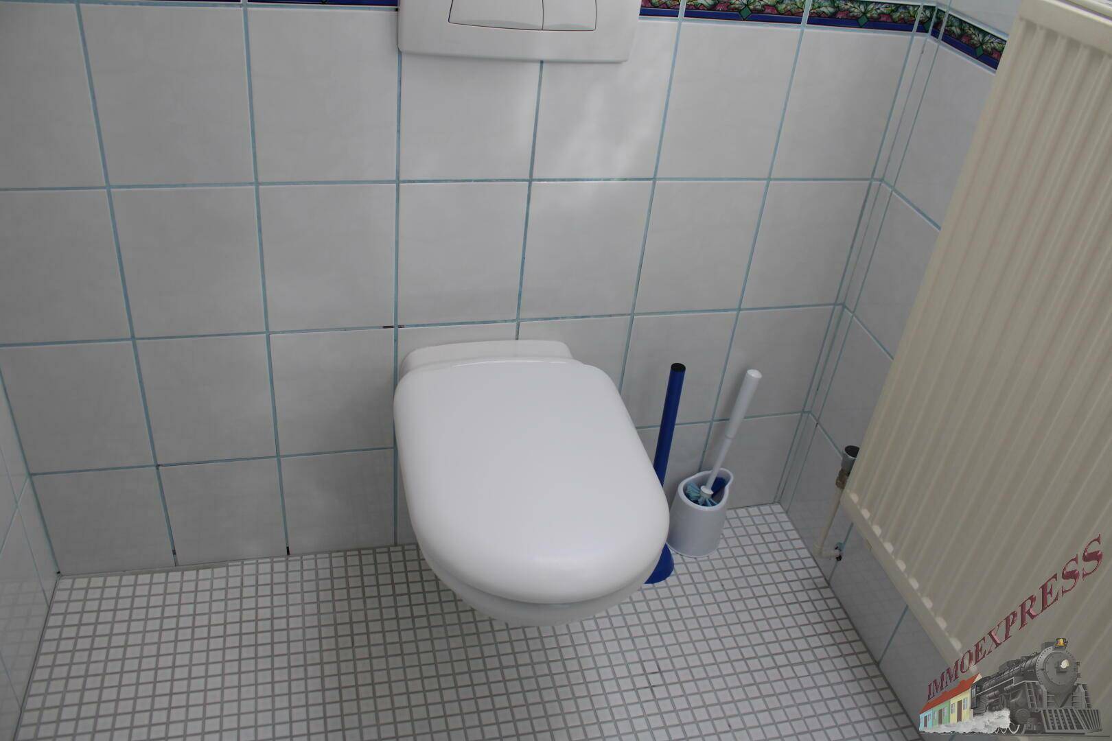 Separate Toilette mit weißen Wand- und Bodenfliesen sowie einem Heizkörper.