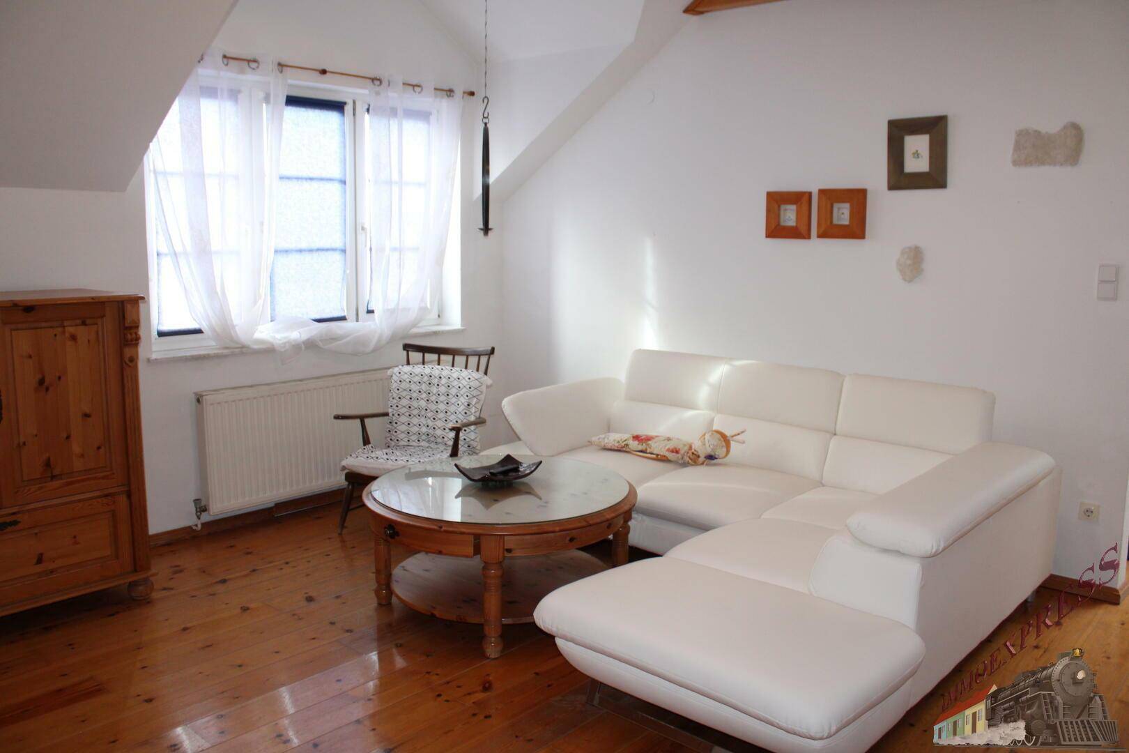 Gemütliches Wohnzimmer im Dachgeschoss mit weißem Sofa, Holzboden und Dachschräge.