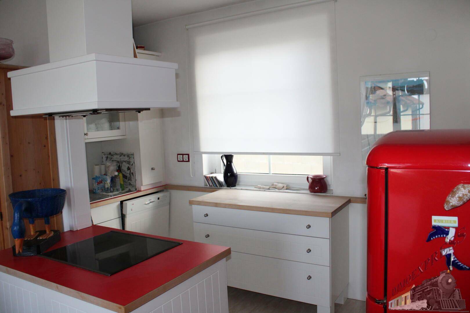 Helle Küche mit rotem Kühlschrank, Induktionskochfeld, Holz-Arbeitsplatten und Fenster.