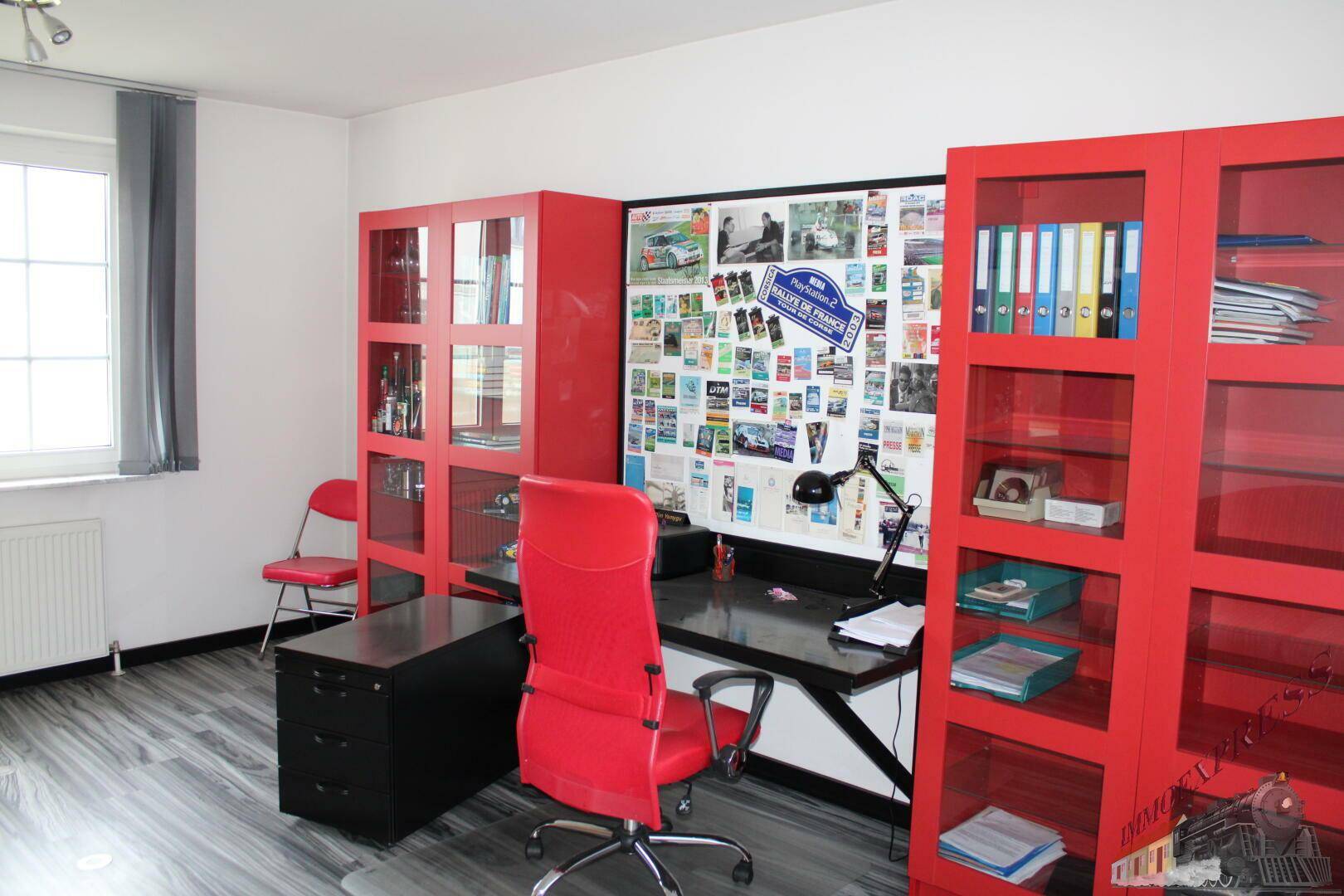 Modernes Büro mit roter Einrichtung, großem Schreibtisch und grauem Laminatboden.