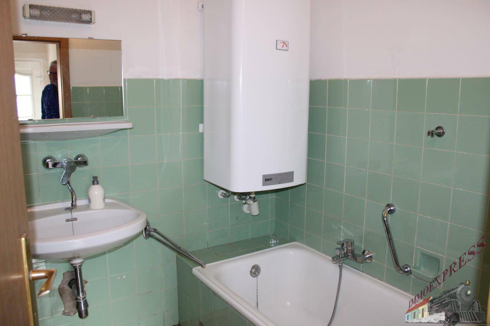 Badezimmer mit Badewanne, Waschbecken und grünen Wandfliesen im 80er-Jahre-Stil.