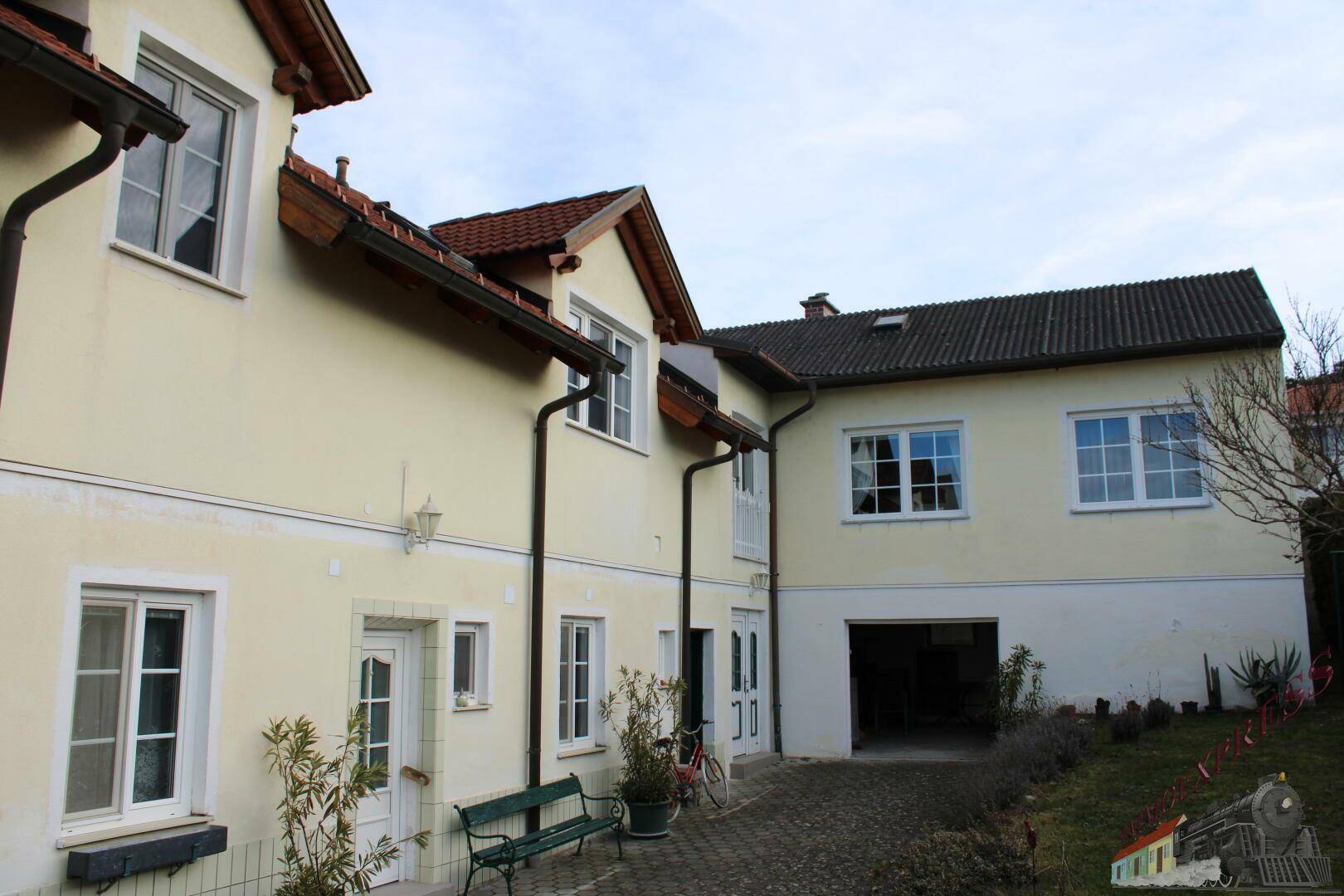 Seitenansicht des Hauses mit gepflastertem Hof, Garagenzufahrt und angrenzendem Gartenbereich.