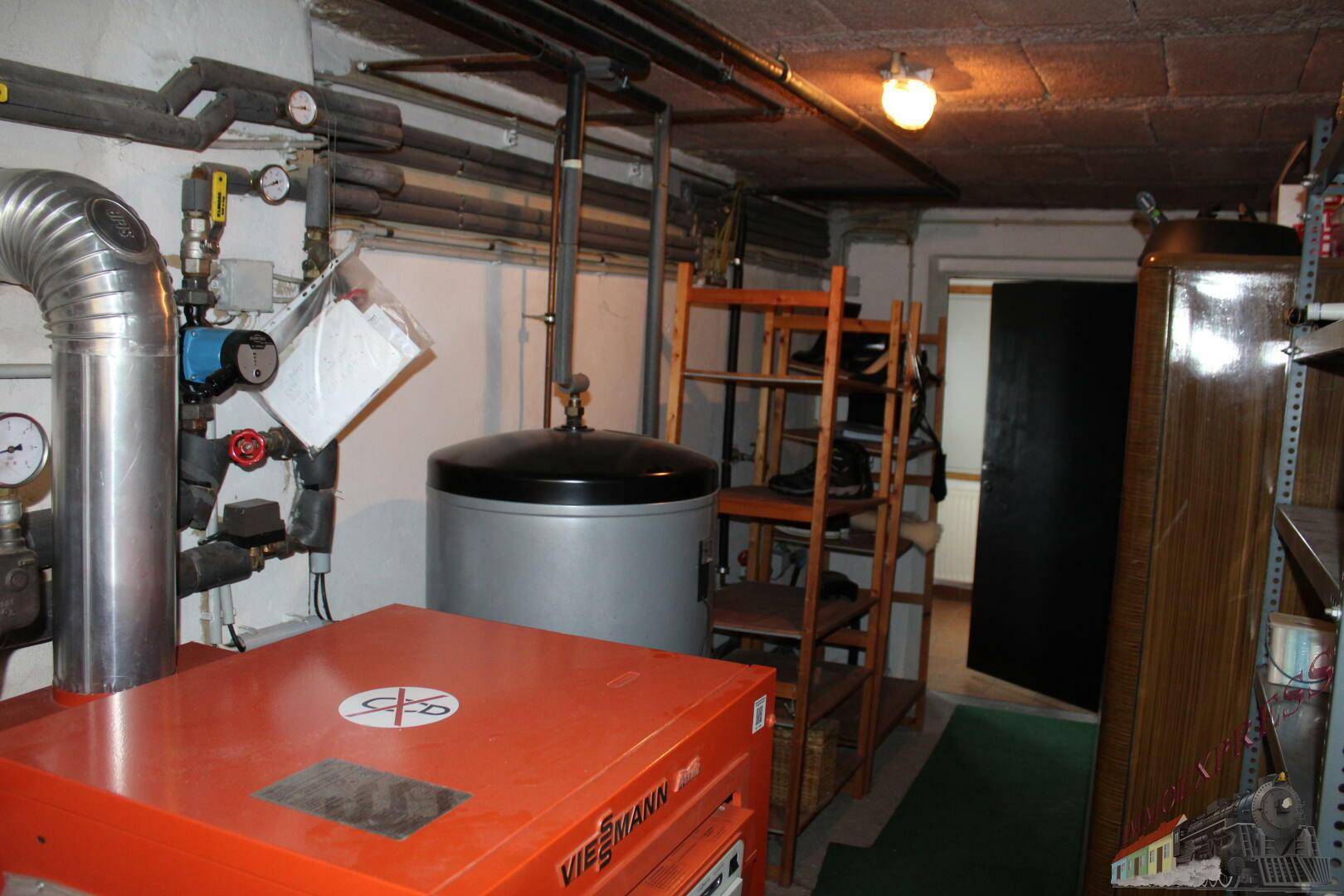 Heizungsraum im Keller mit Warmwasserspeicher, Rohrsystem und Lagerregalen.