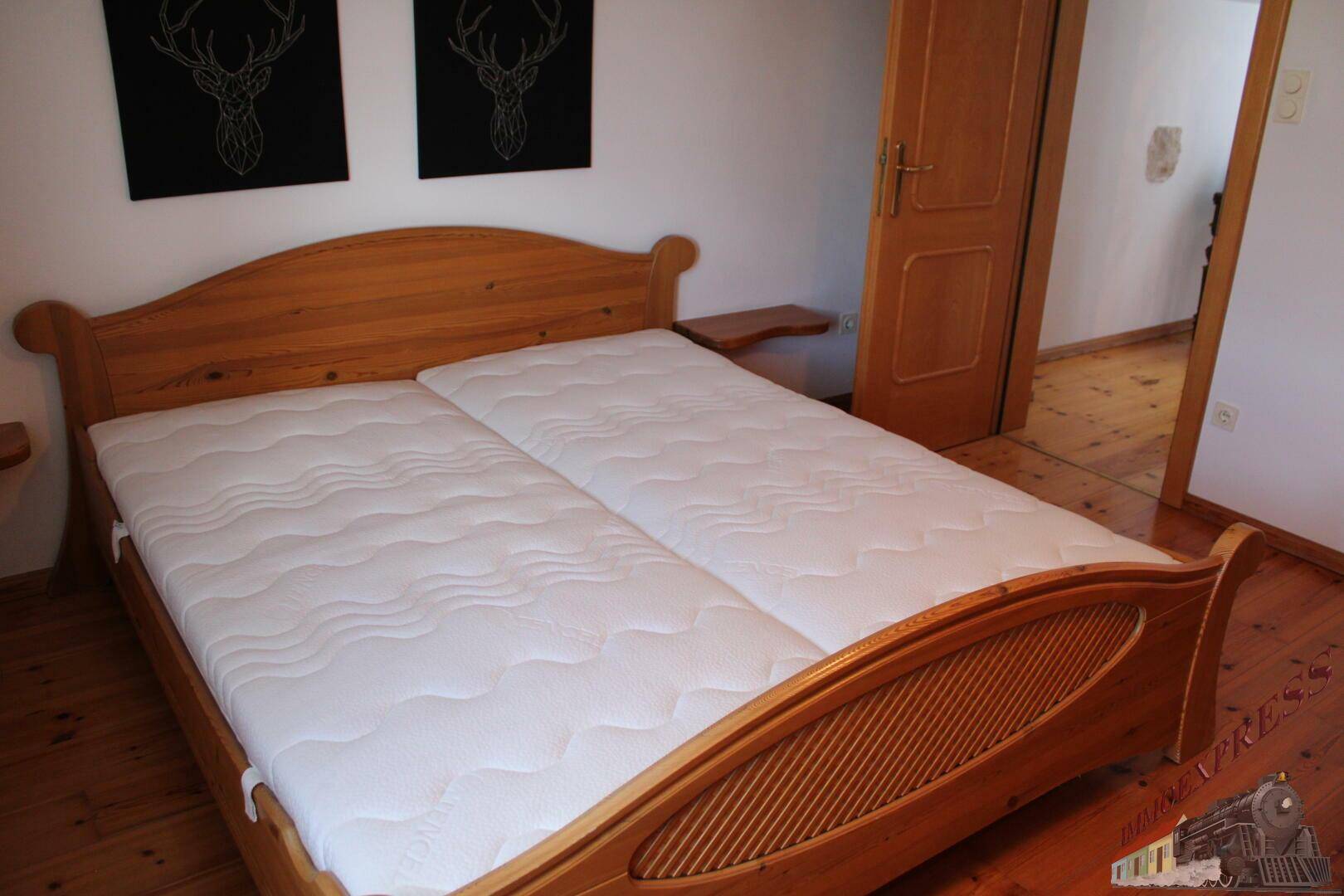 Schlafzimmer mit hellem Holzbett, Holzboden und einfacher Einrichtung, durch eine Tür zugänglich.