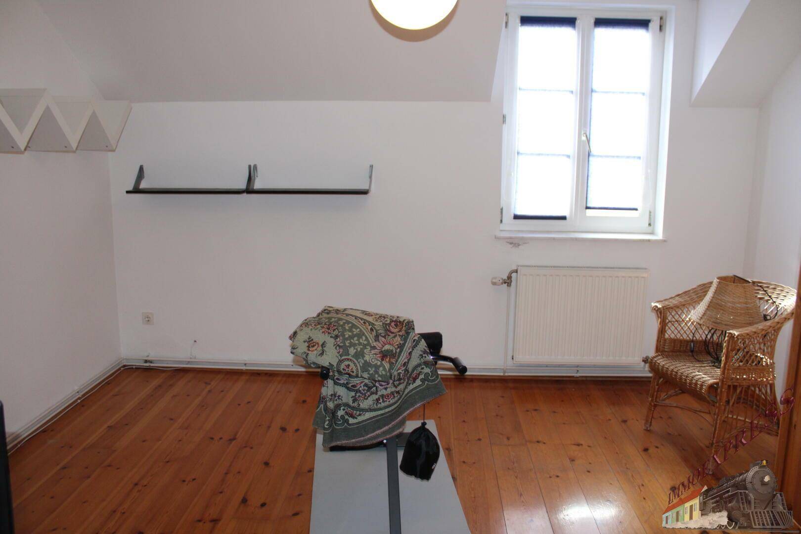 Helles Zimmer im Dachgeschoss mit Holzboden, Dachschräge und einem Fenster für natürliche Belichtung.
