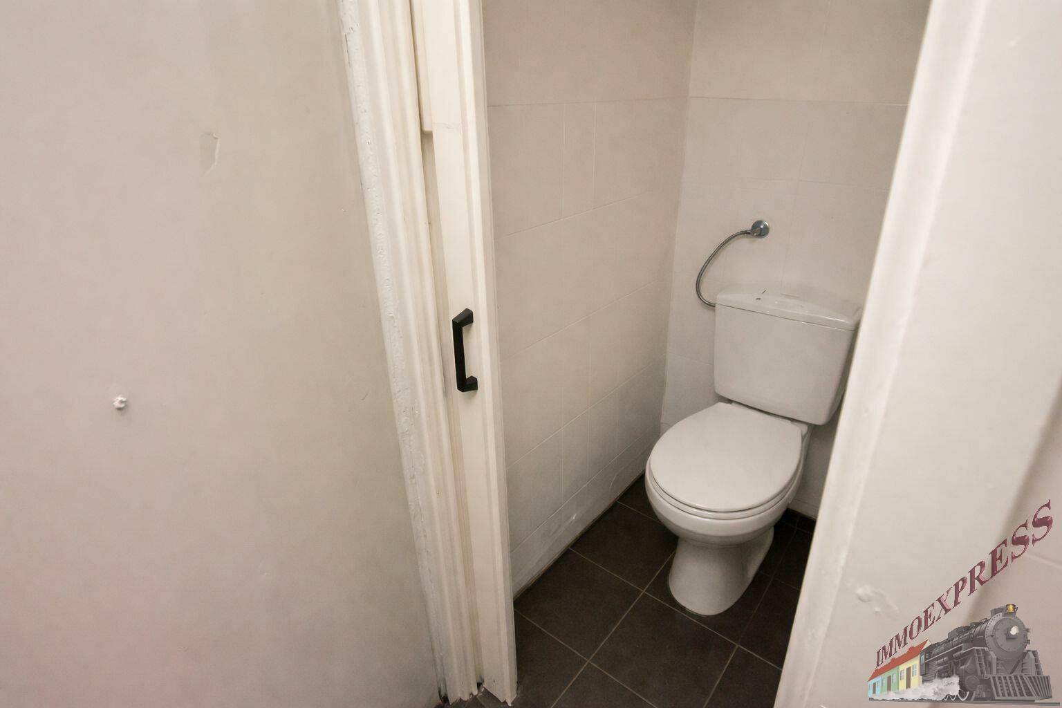 Kleiner, funktionaler Toilettenraum mit weißen Fliesen und dunklem Boden, der einen sauberen Eindruck macht.