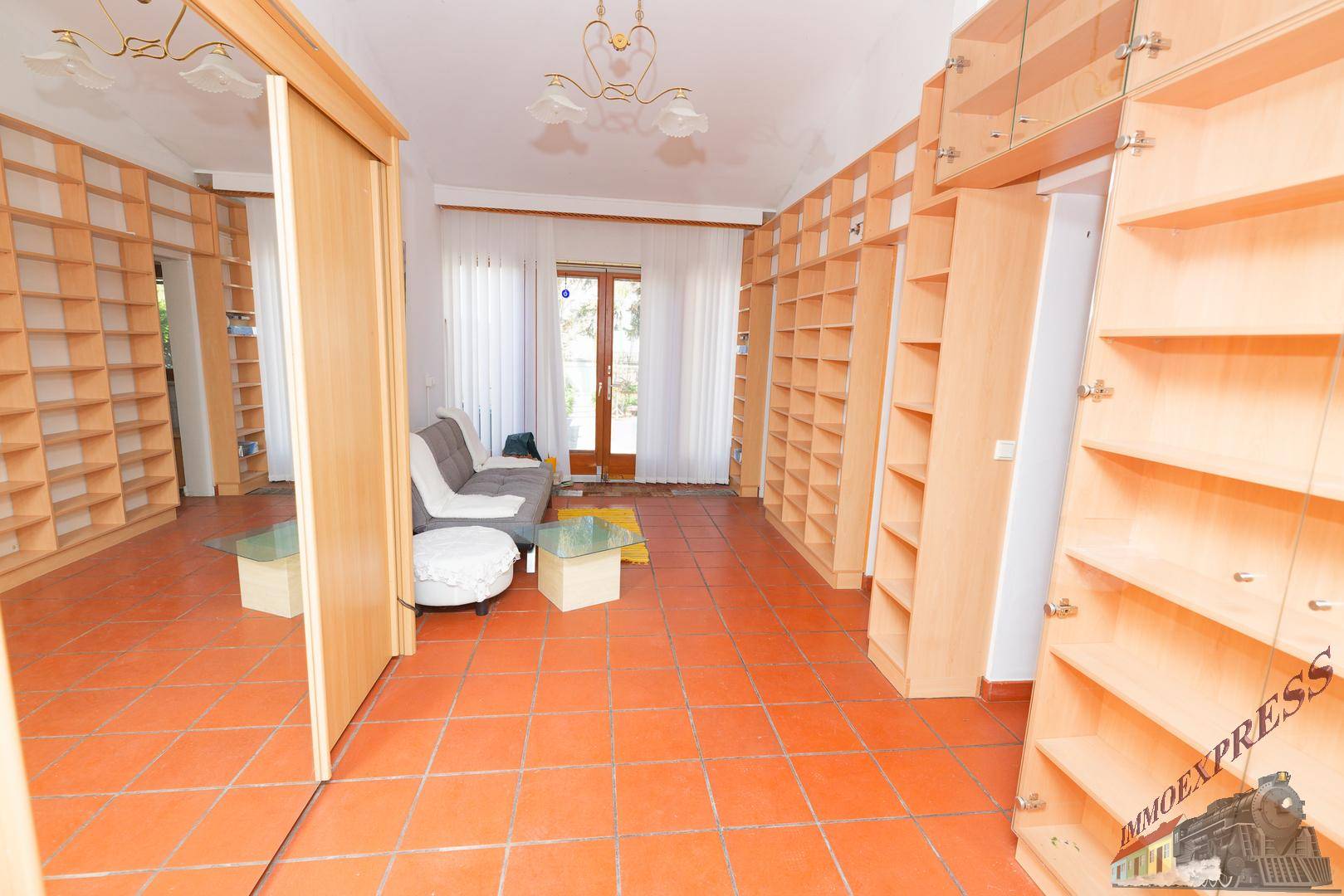 Geräumiger Wohnbereich mit vielen Bücherregalen, Terrakottafliesen und Terrassenzugang.