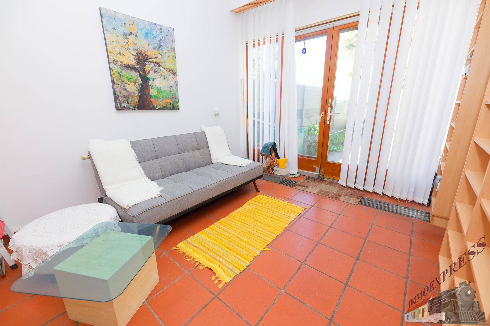Gemütliches Wohnzimmer mit Terrakottafliesen, Sofa und Zugang zum Außenbereich.