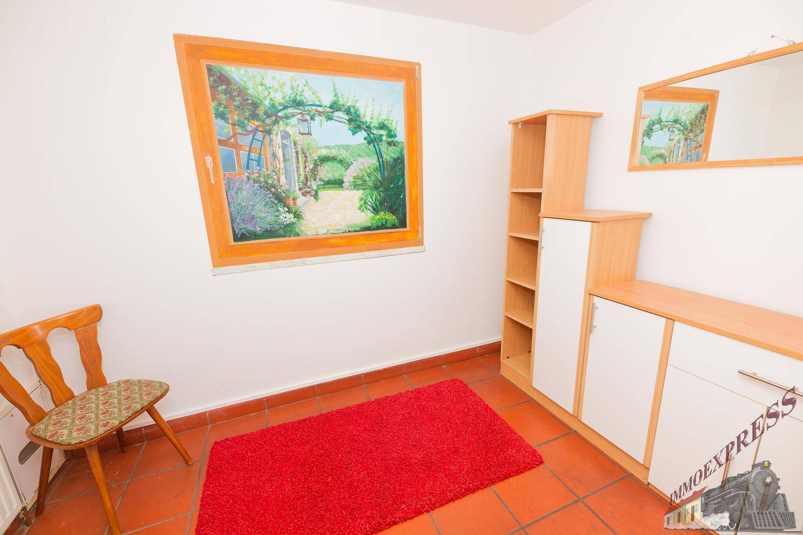 Raum mit Holzmöbeln, Spiegel und rotem Teppich auf Terrakottafliesen.