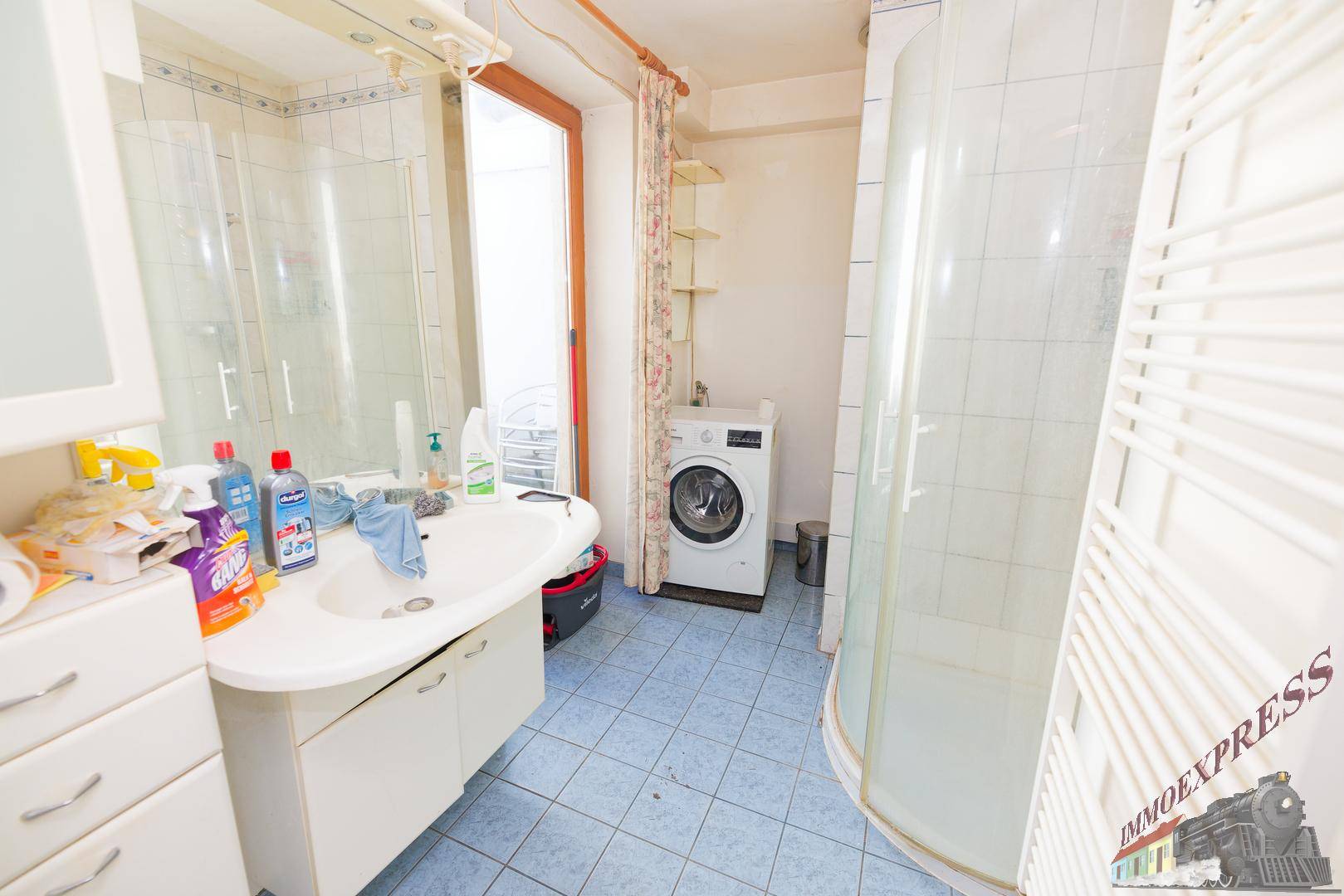 Badezimmer mit Dusche, Waschbecken und Waschmaschine auf blauen Fliesen.