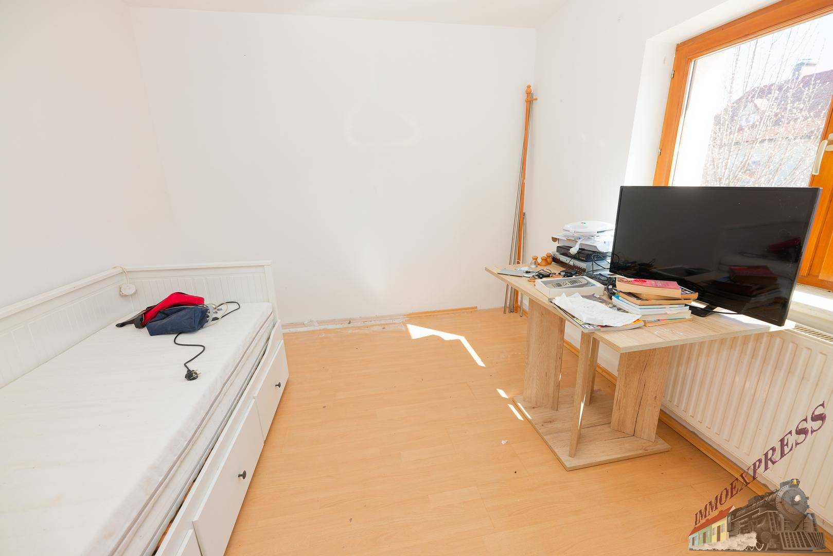 Schlafzimmer mit hellem Laminatboden, Einzelbett und Fenster.