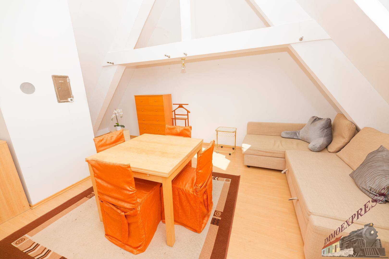 Heller Dachbodenbereich mit Holzbalken, Essplatz und Sofa auf Laminatboden.