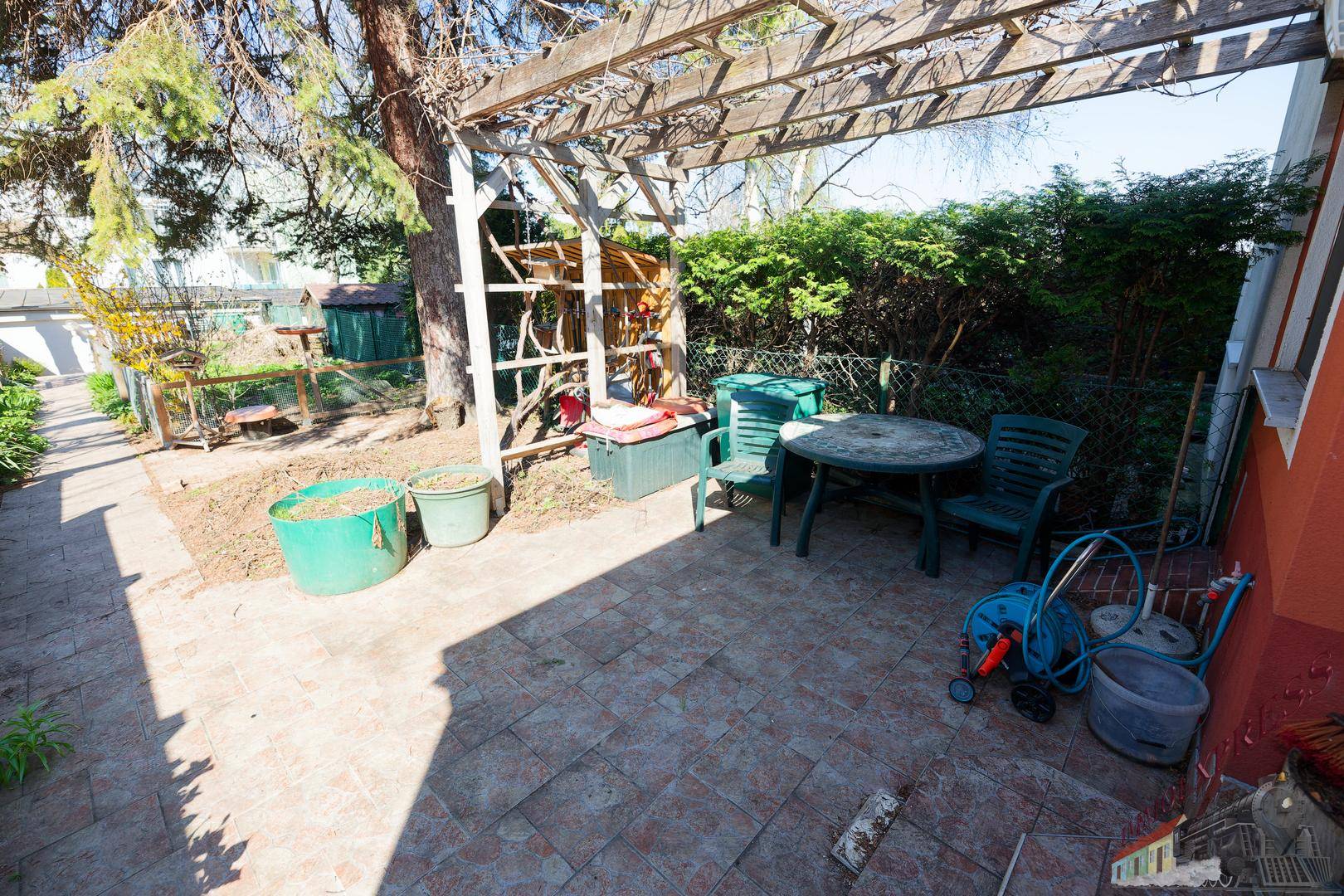 Große gepflasterte Terrasse mit Gartenmöbeln und schattenspendender Pergola.
