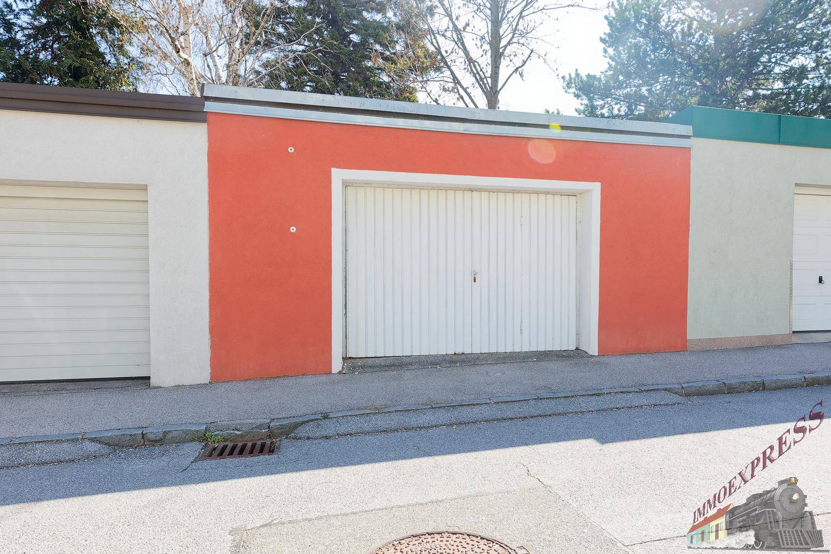 Einzelgarage mit weißem Tor und orangefarbener Fassade an der Straße.