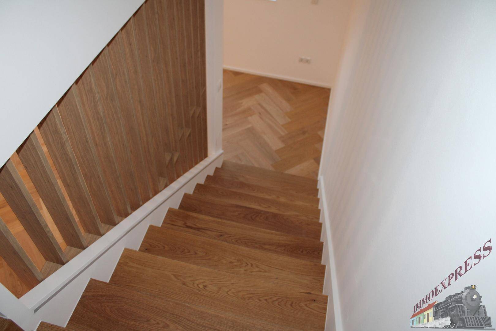 Moderne Holztreppe mit stilvollem Holzgeländer und Fischgrätparkett im unteren Bereich.