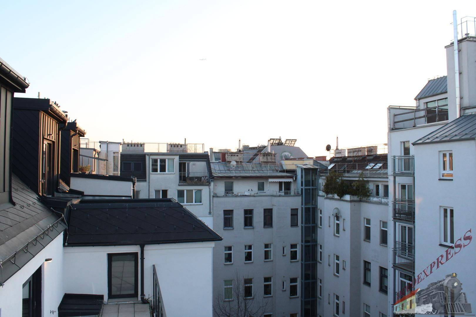 Blick über die Dächer der Stadt mit verschiedenen Gebäuden und einem Aufzug an der Fassade.