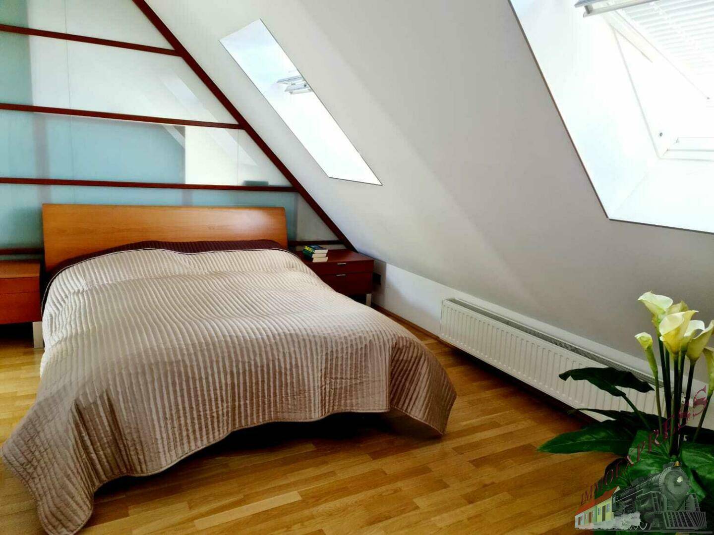 Schlafzimmer im Dachgeschoss mit schrägen Wänden, Dachfenstern und einem großen Bett.