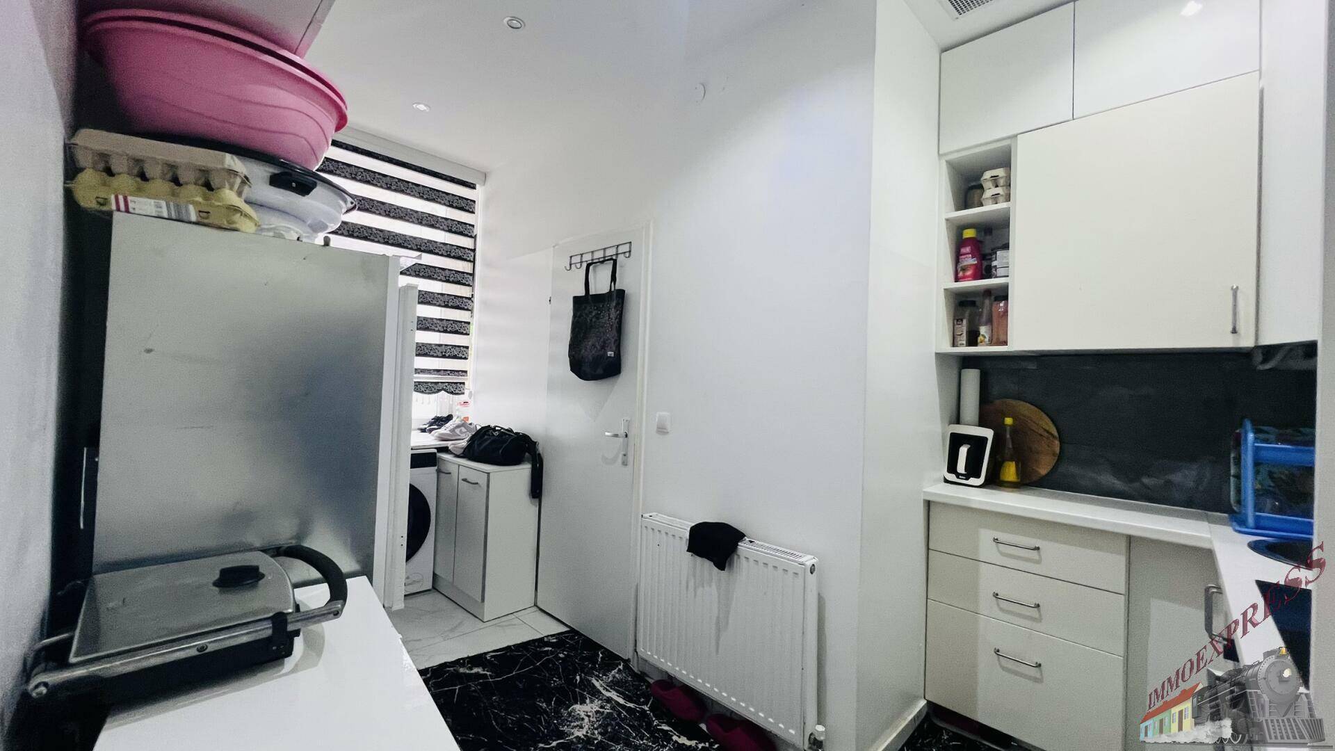 Funktionale Küche mit weißen Schränken, Kühlschrank und Waschmaschine auf Marmorfliesen.