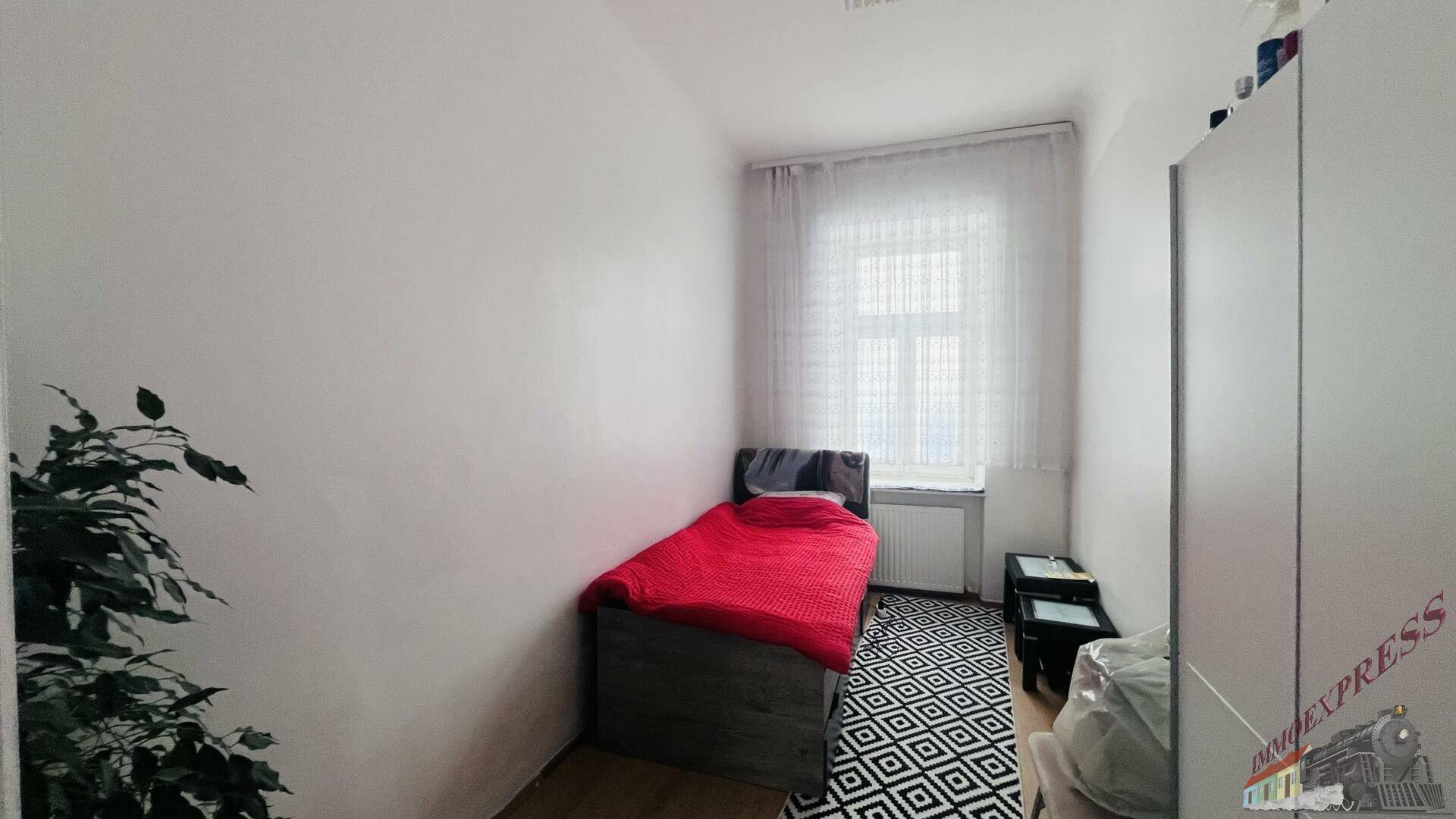 Kleines Schlafzimmer mit Einzelbett, Fenster und gemustertem Teppich auf Holzfußboden.