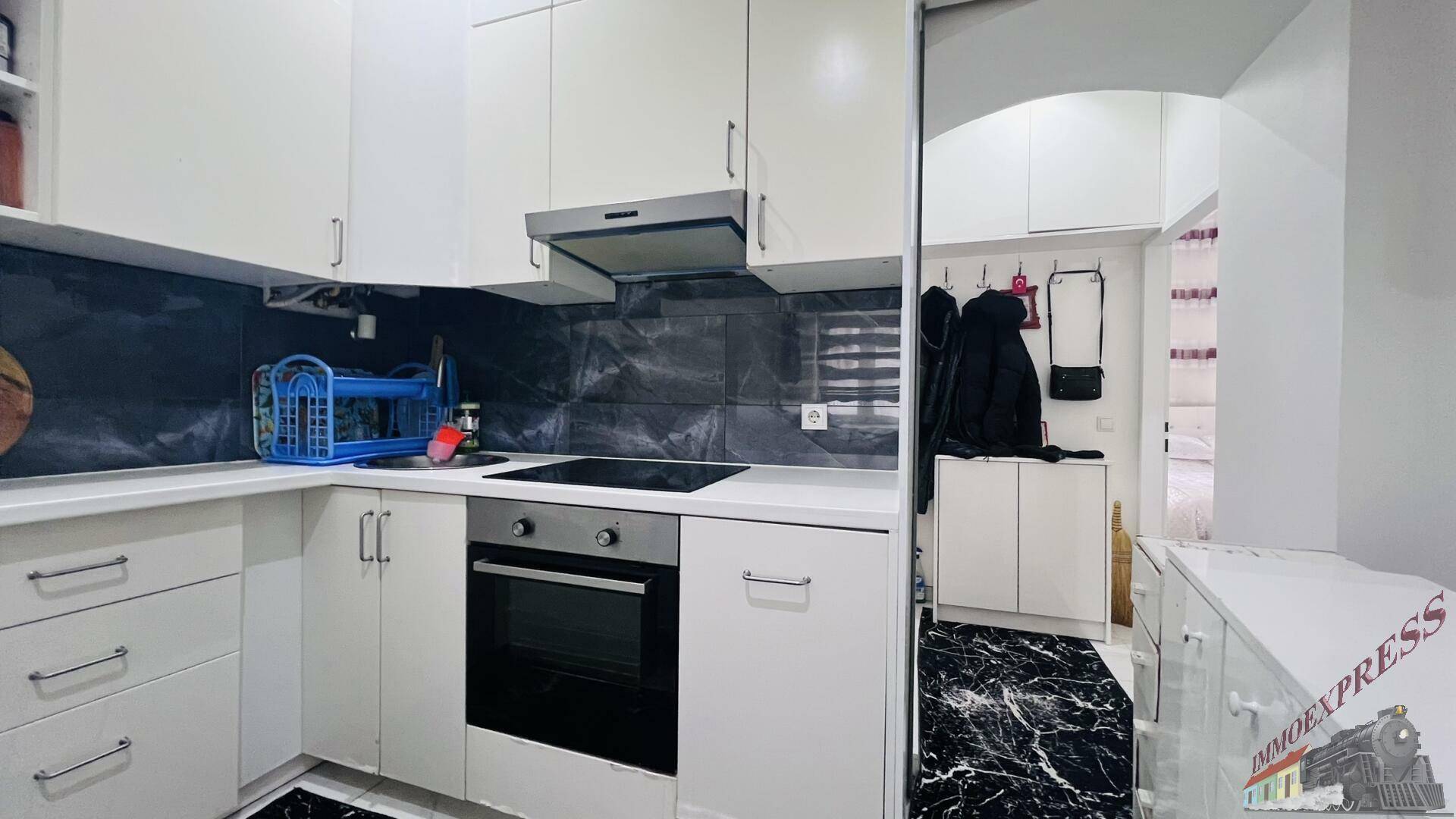 Moderne Einbauküche mit weißen Schränken, Induktionskochfeld und Backofen auf Marmorfliesen.