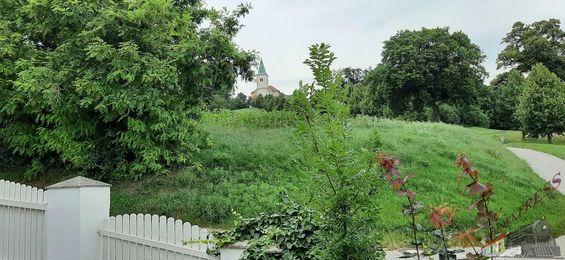 Malerischer Blick auf eine Kirche auf einem grünen Hügel, umgeben von Bäumen.