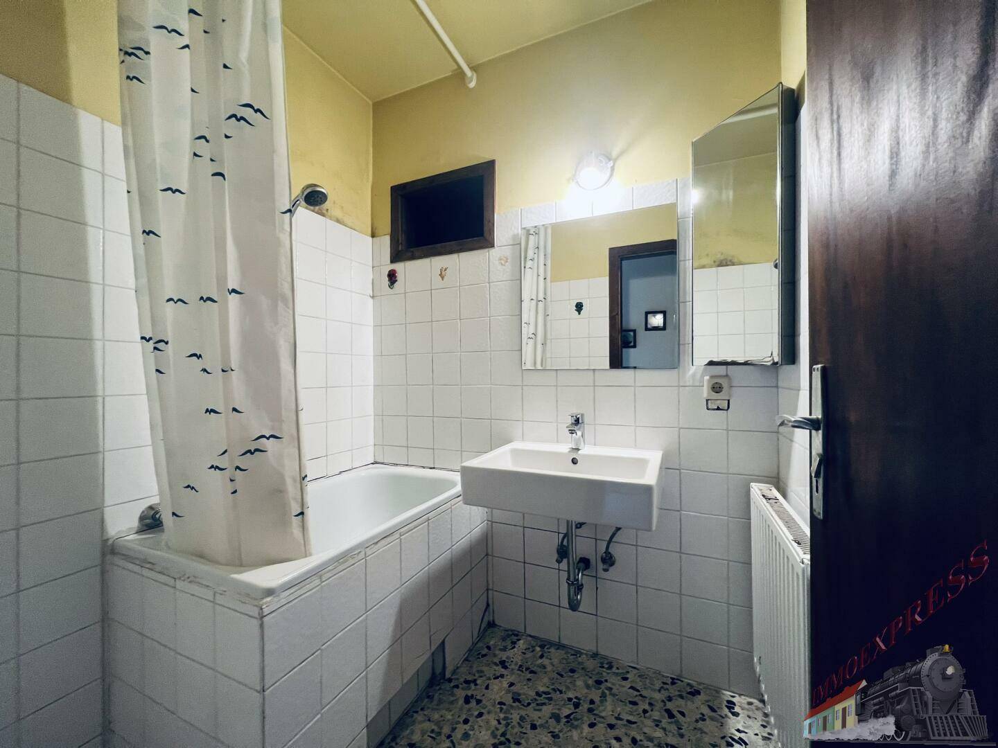Badezimmer mit Badewanne, Fliesenwänden und einem Waschbecken mit Spiegel.
