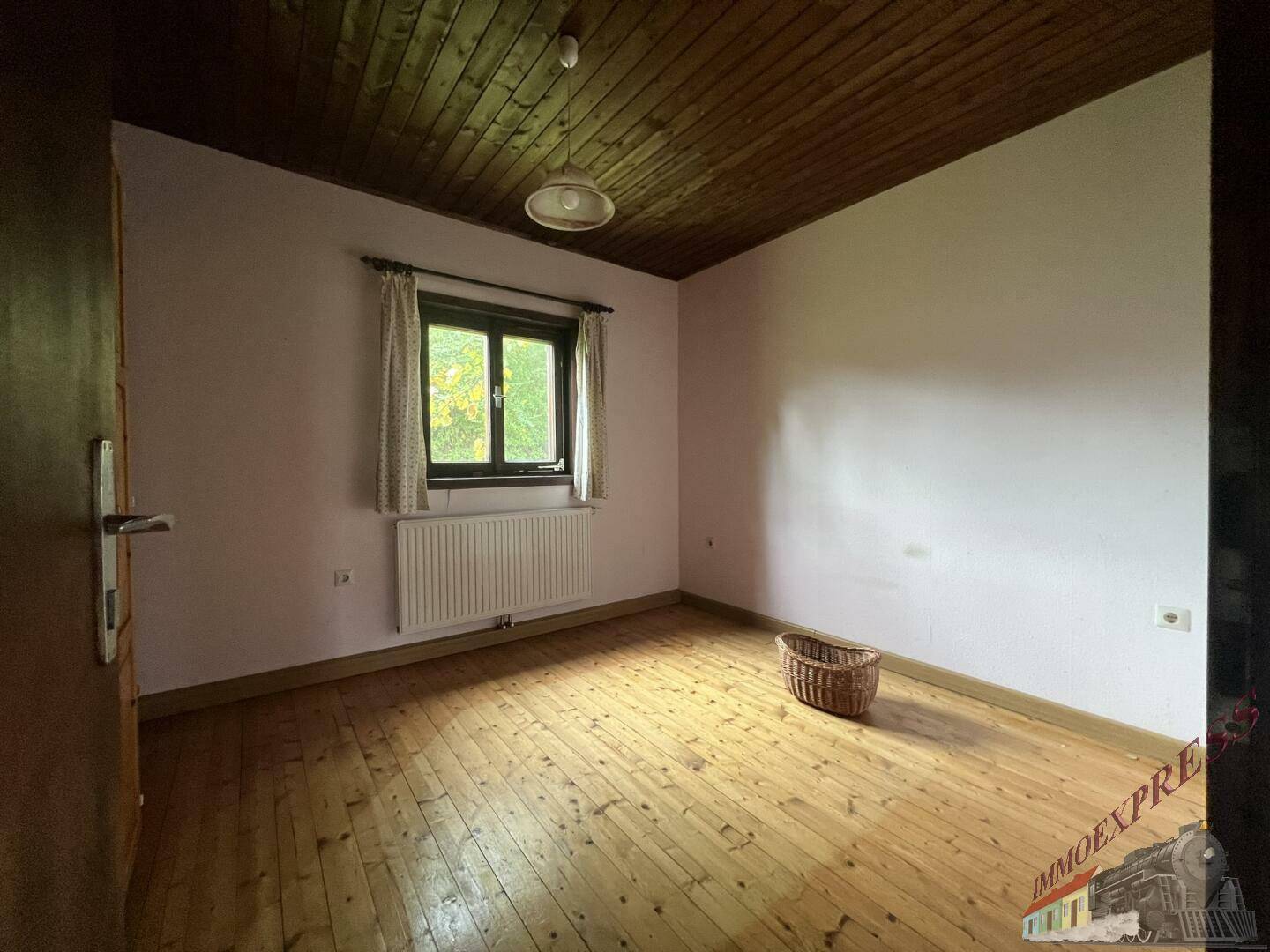 Schlafzimmer mit Holzdielenboden, Holzdecke und einem Fenster, das viel Licht hereinlässt.
