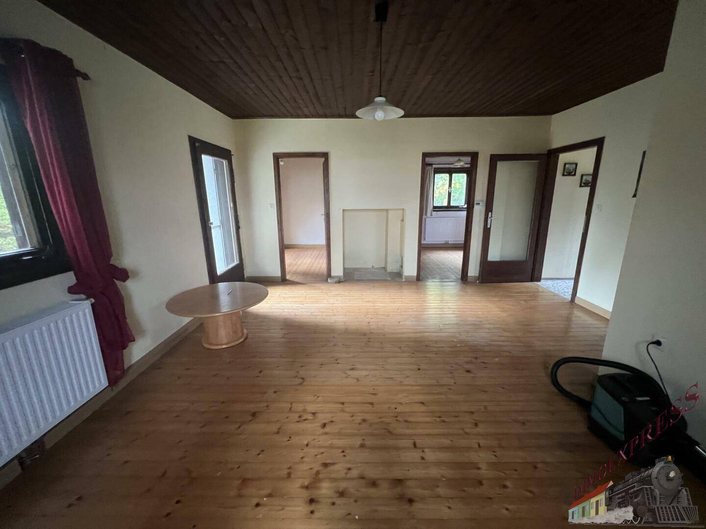 Helles Wohnzimmer mit Holzdielenboden, Holzdecke und Blick auf mehrere Zimmertüren.