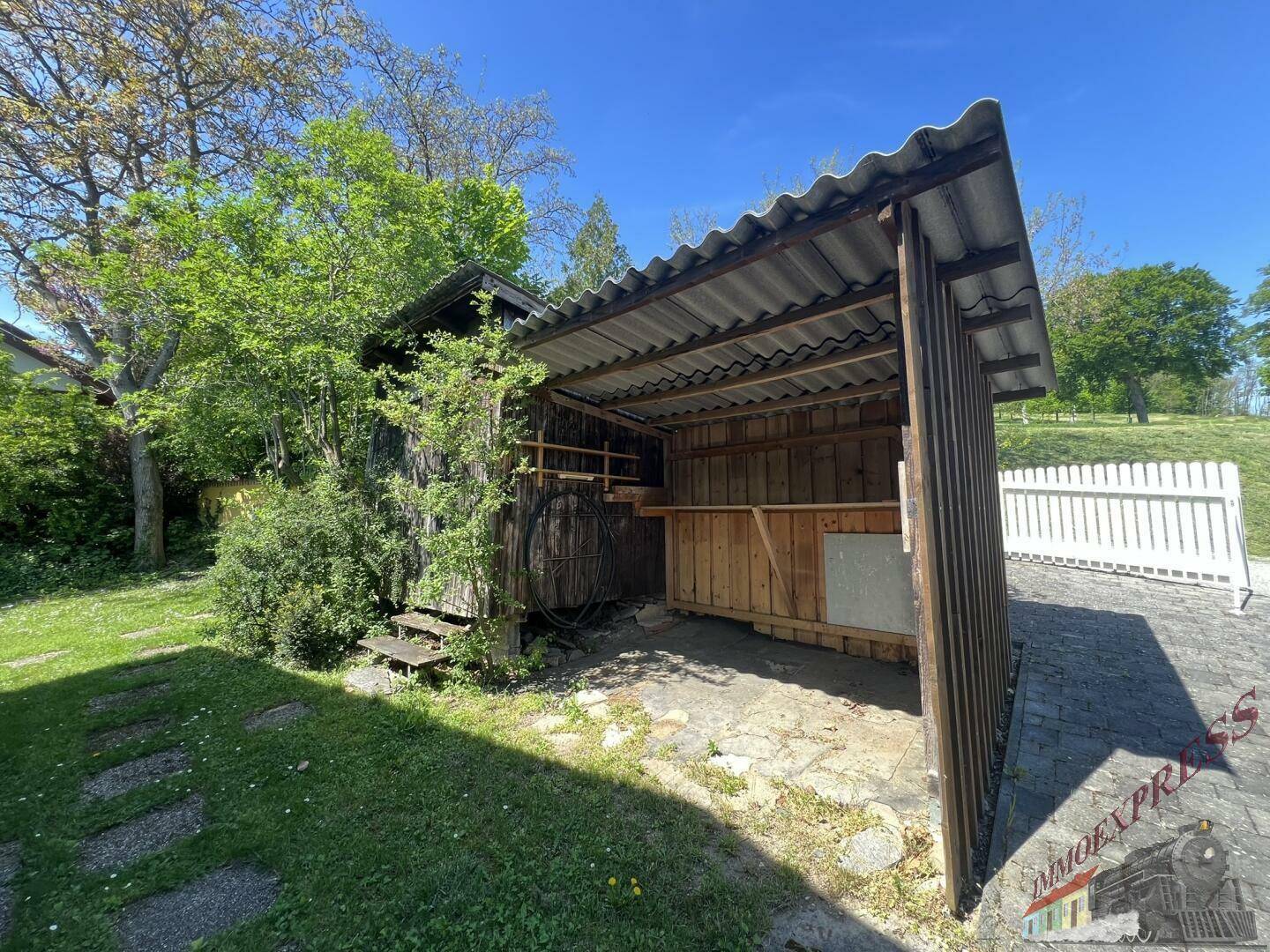 Offener Holzschuppen mit Wellblechdach und angrenzender Rasenfläche.
