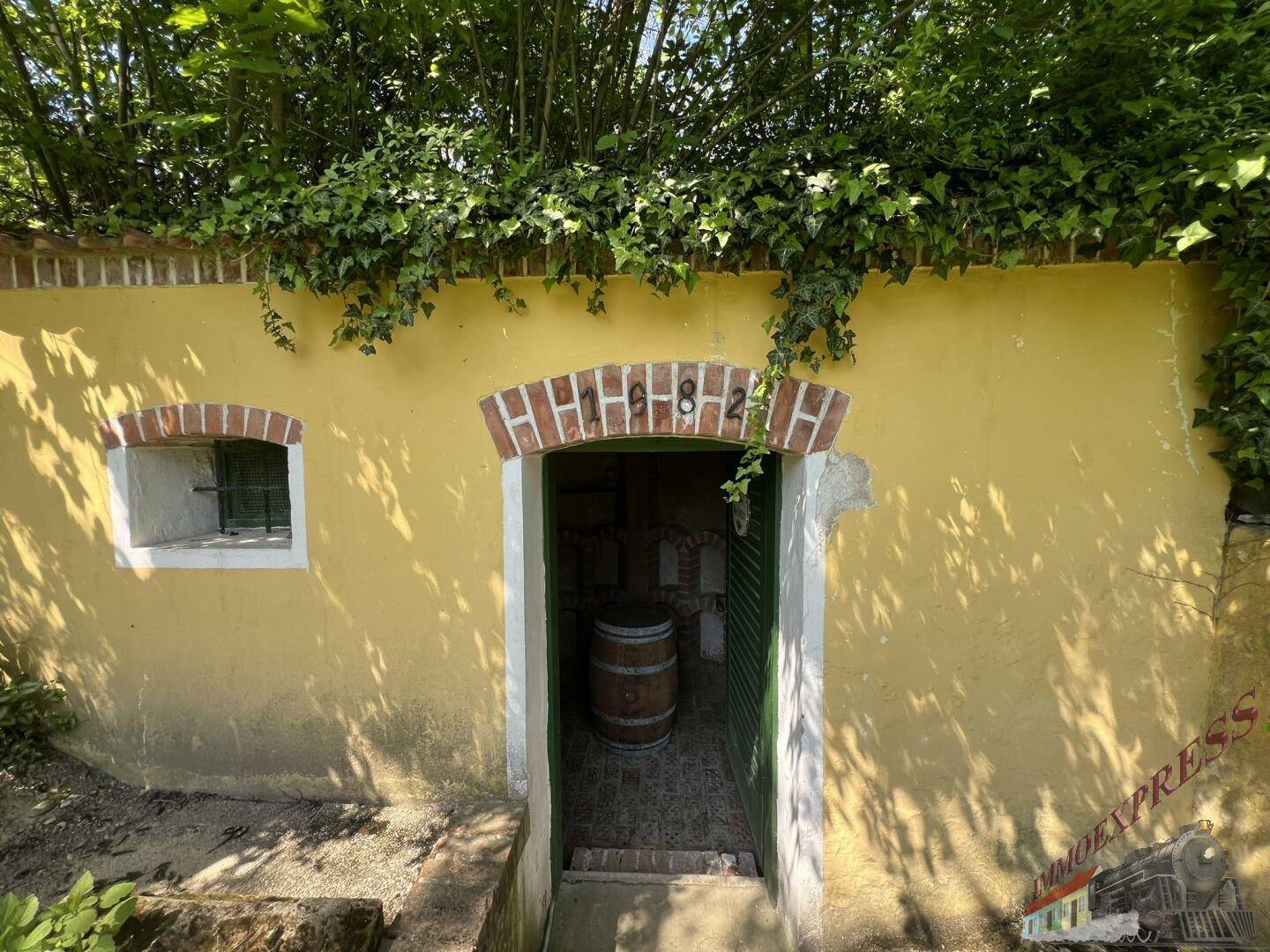Eingang zum historischen Weinkeller mit gelber Fassade, Ziegelbogen und der Jahreszahl 1882.