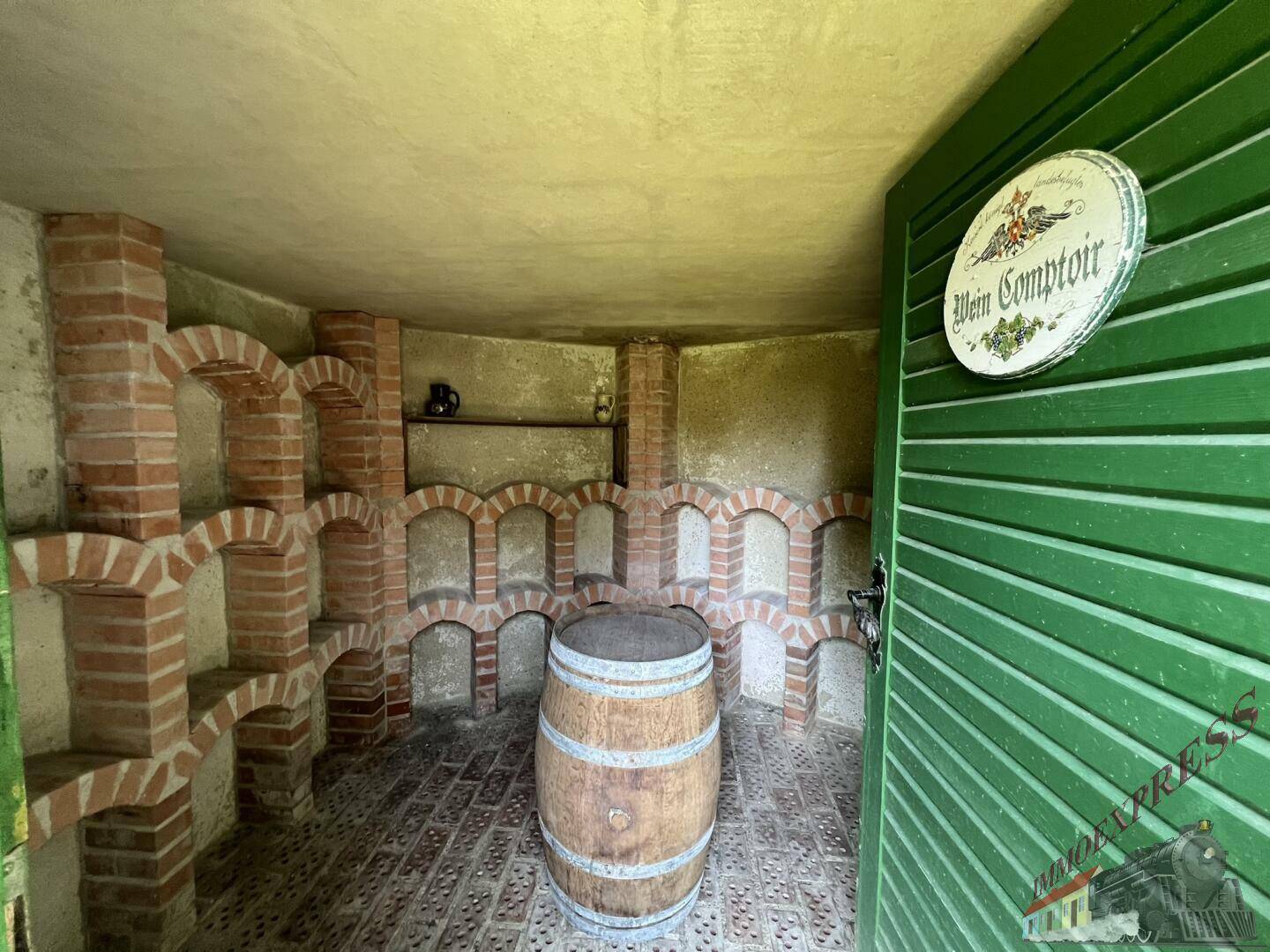 Rustikaler Weinkeller mit Ziegelbögen, Holzfass und traditionellem Schild an der Tür.