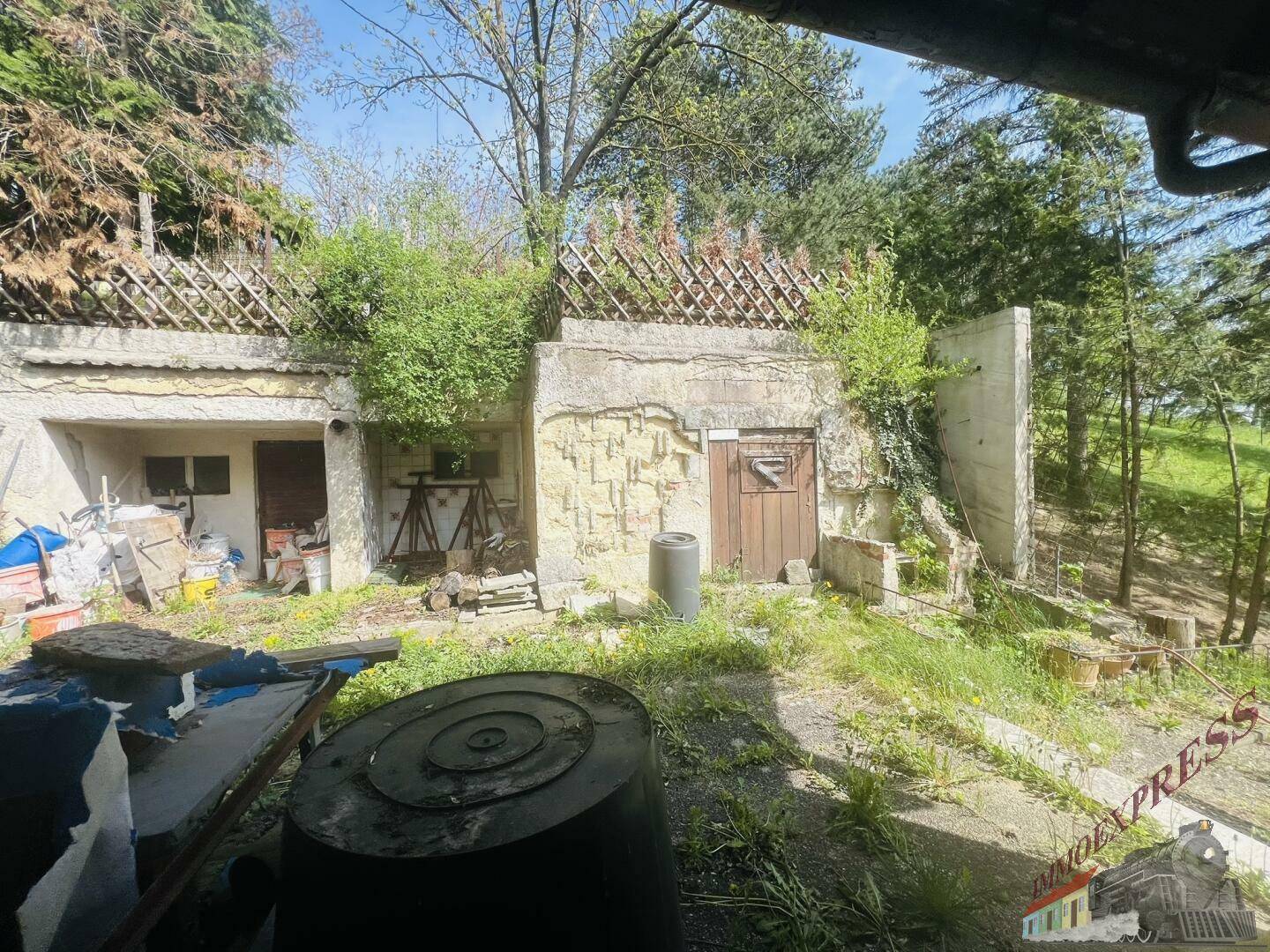 Alte, in den Hang gebaute Struktur mit Holztür und überwuchertem Bereich.