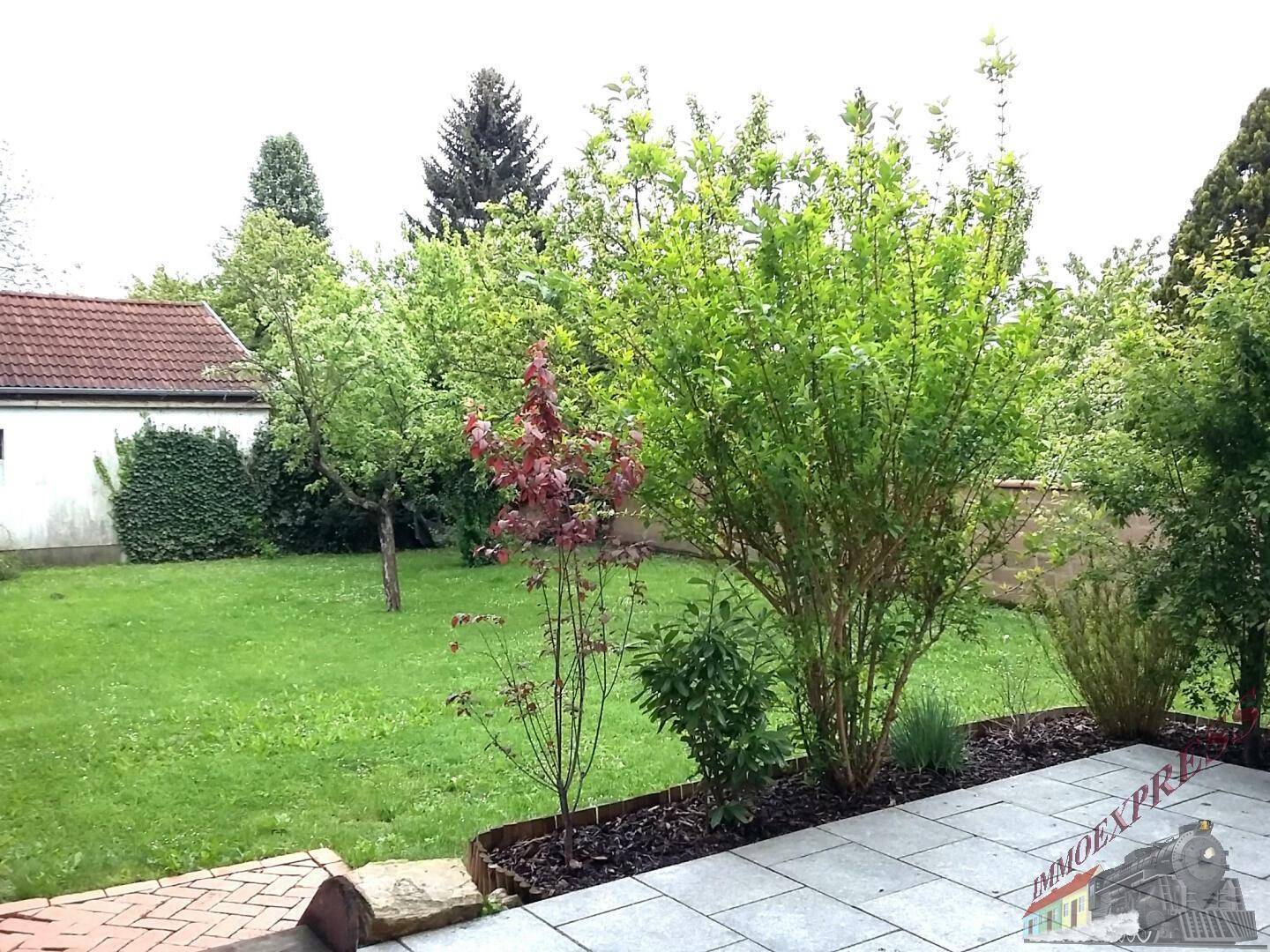 Gepflegter Gartenbereich mit Rasen, Sträuchern und einer modernen gepflasterten Terrasse.