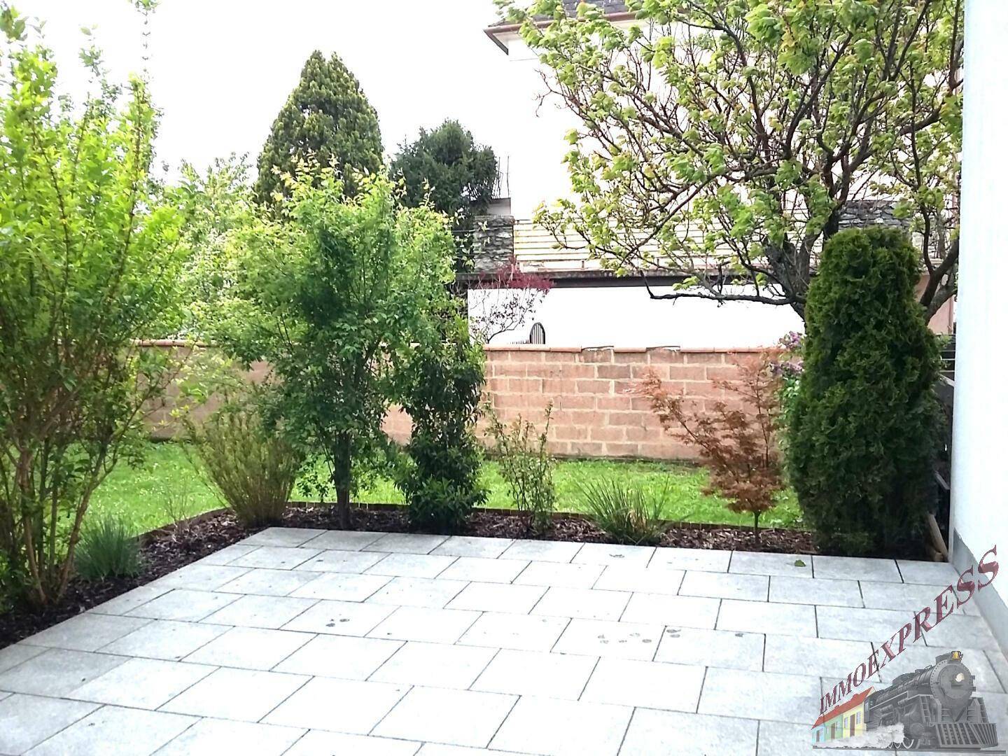 Gepflegter Gartenbereich mit Rasen, Sträuchern und einer modernen gepflasterten Terrasse.