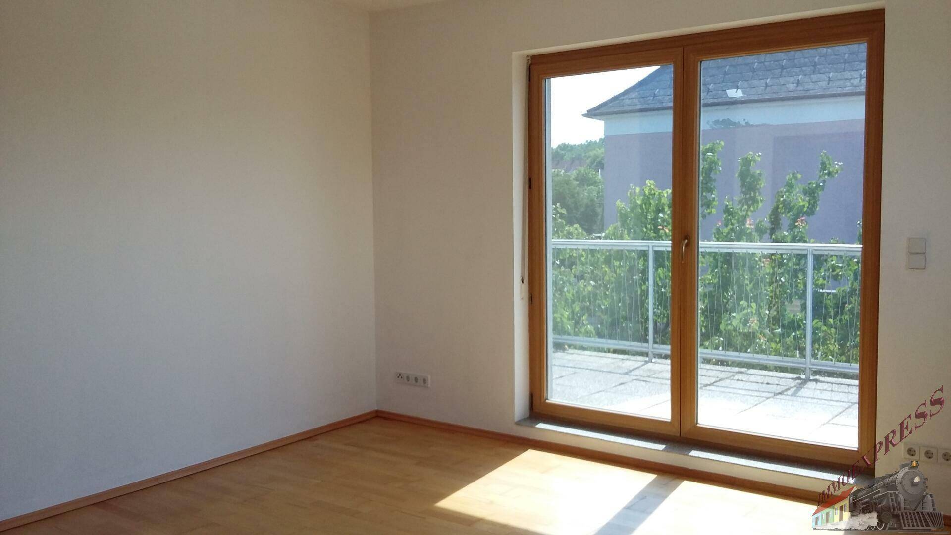 Leerer Raum mit hellem Parkettboden und großem Fenster mit Zugang zu einem französischen Balkon.