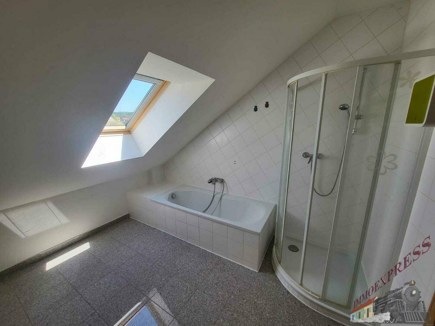 Helles Dachgeschossbad mit Badewanne, Duschkabine, Dachfenster und Fliesenboden.