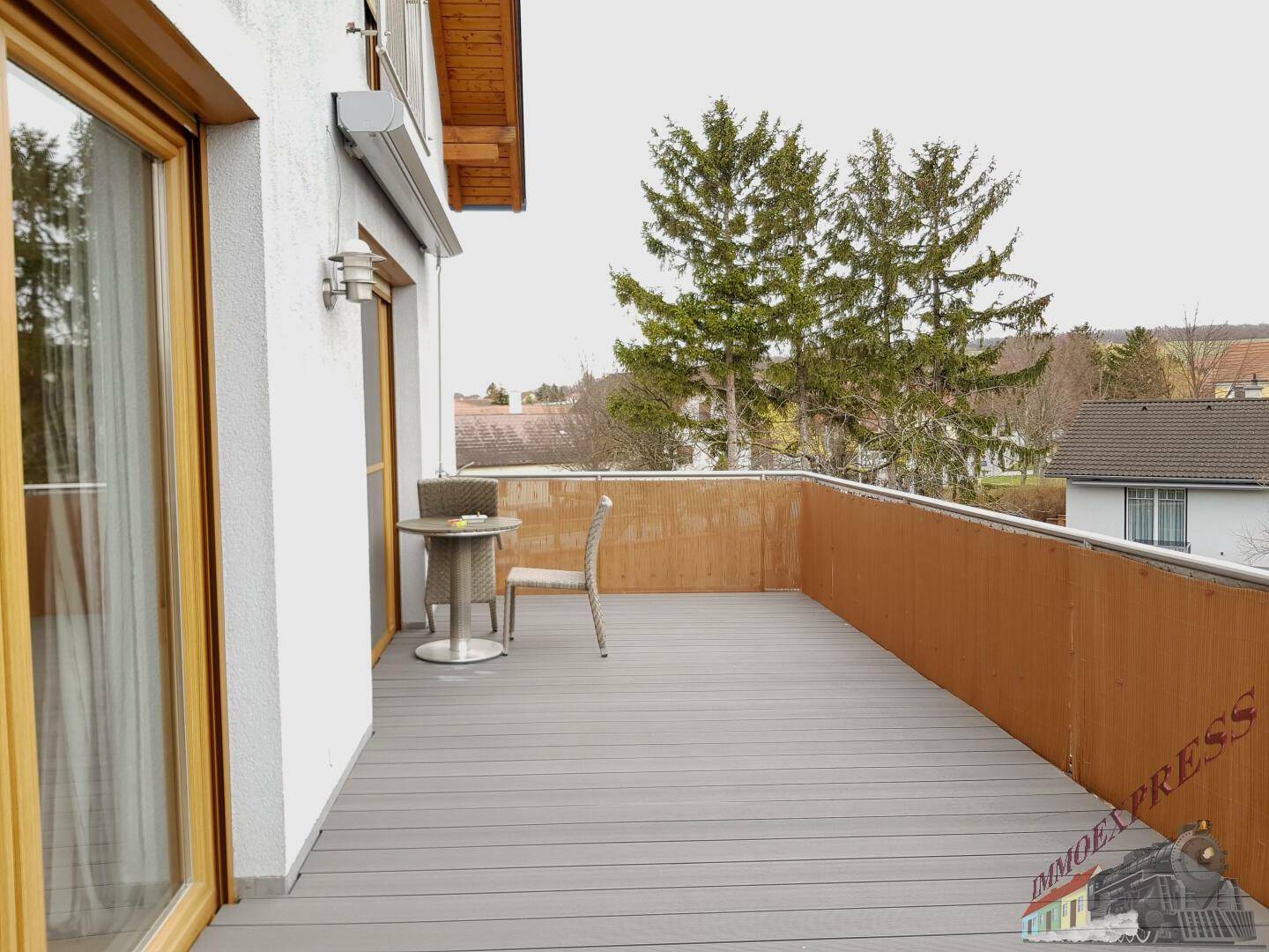 Geräumiger Balkon mit Holzboden und Sitzgelegenheiten, umgeben von grüner Landschaft.