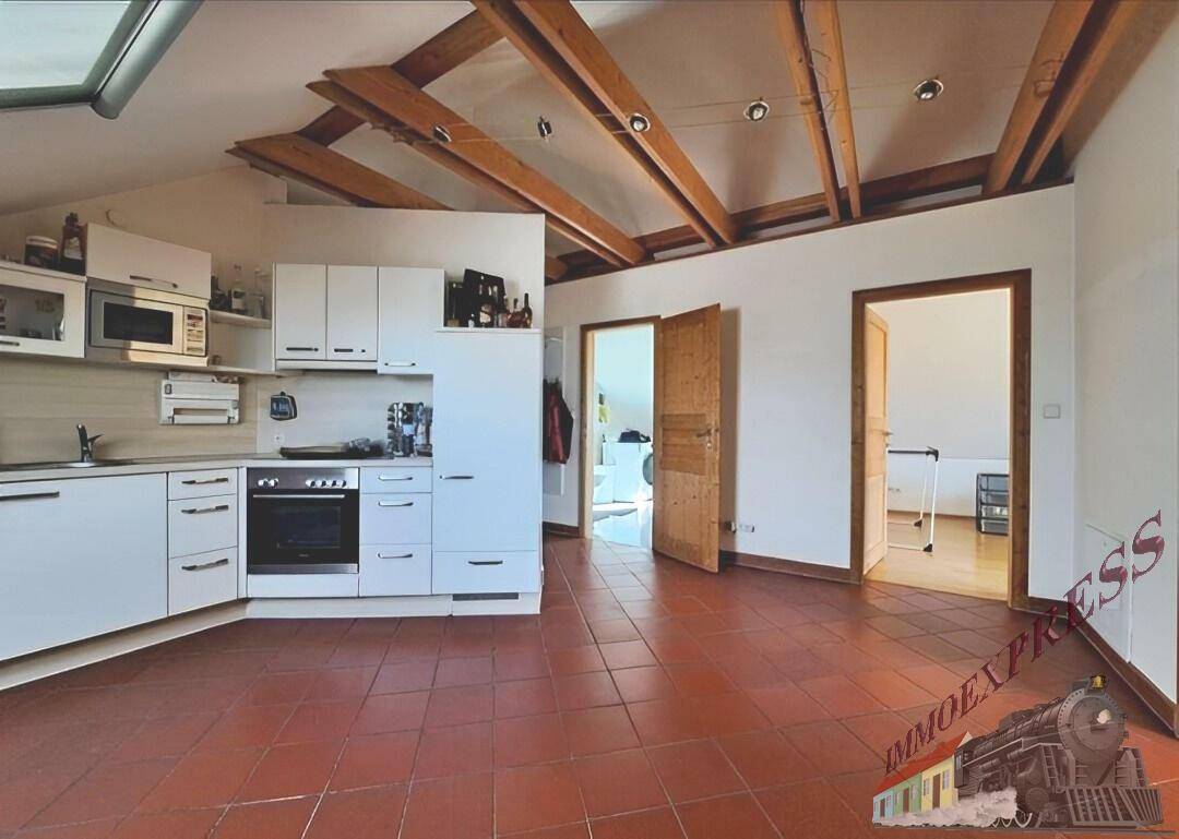 Helle Küche im Dachgeschoss mit sichtbaren Holzbalken, Terrakottafliesen und Dachfenster.