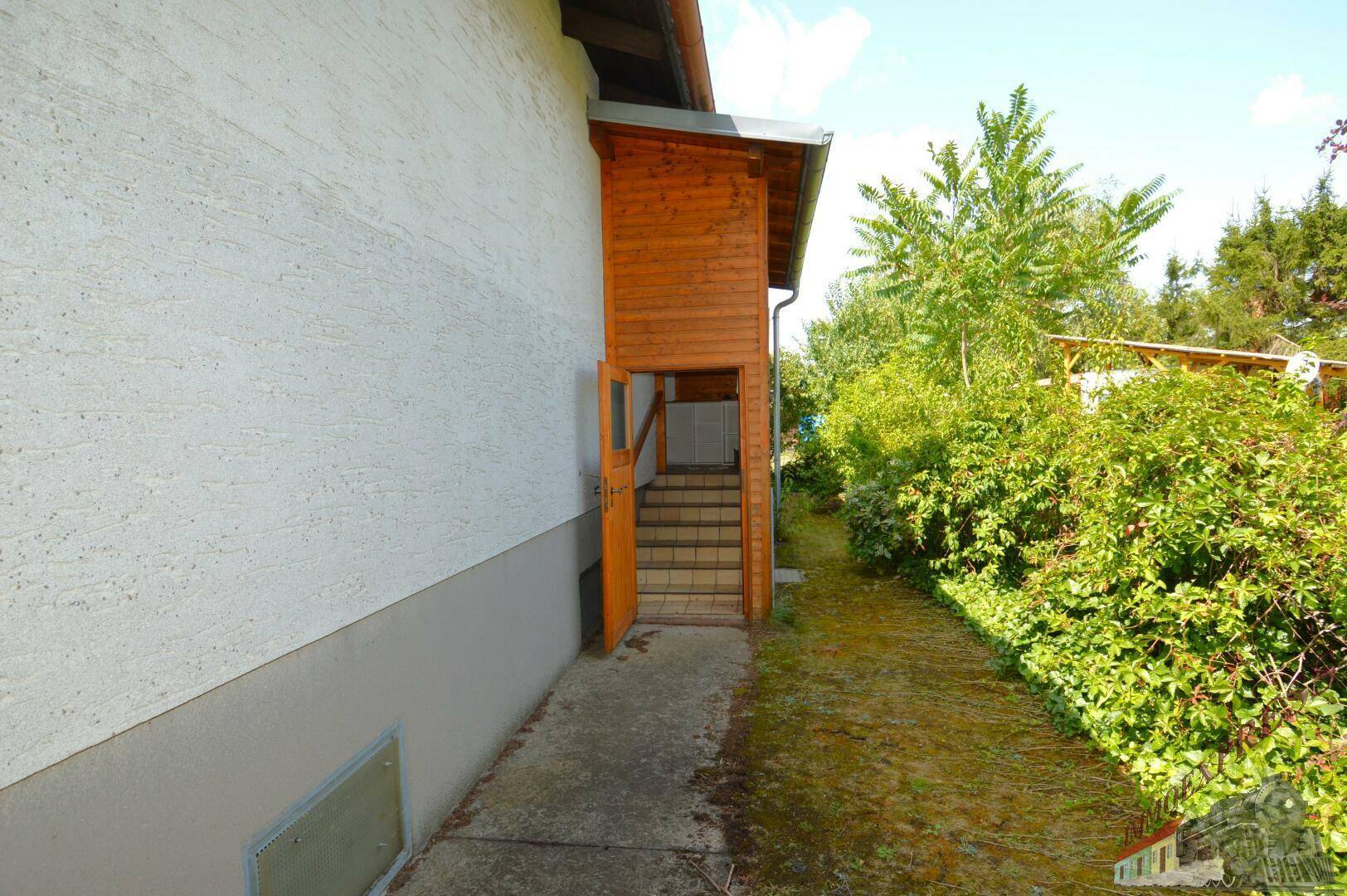 Seitlicher Zugang zum Haus mit Holztreppe und üppiger Vegetation im Gartenbereich.
