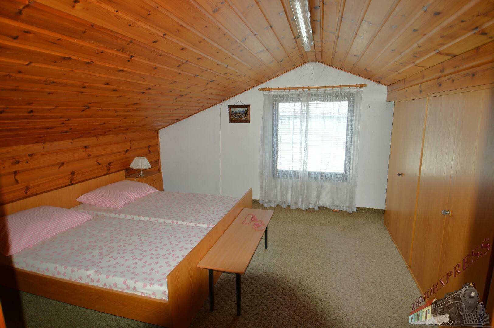 Gemütliches Schlafzimmer im Dachgeschoss mit Holzvertäfelung und Teppichboden.