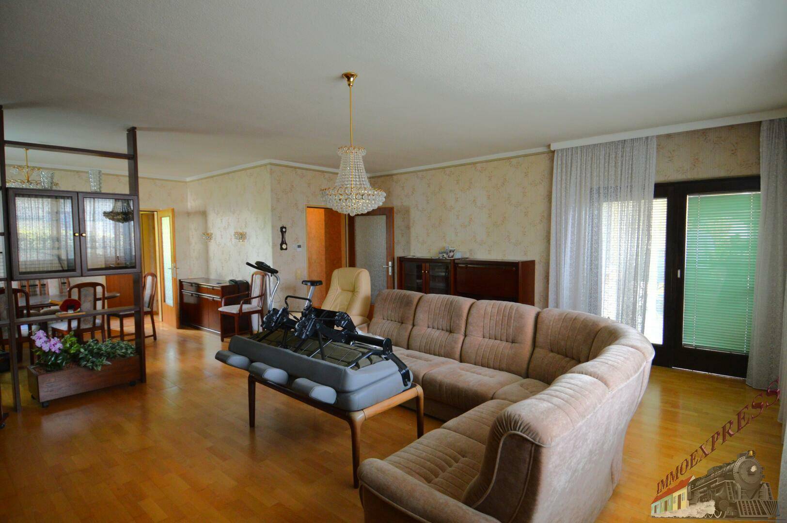 Geräumiger Wohn- und Essbereich mit Parkettboden, großer Couch und Kronleuchter.