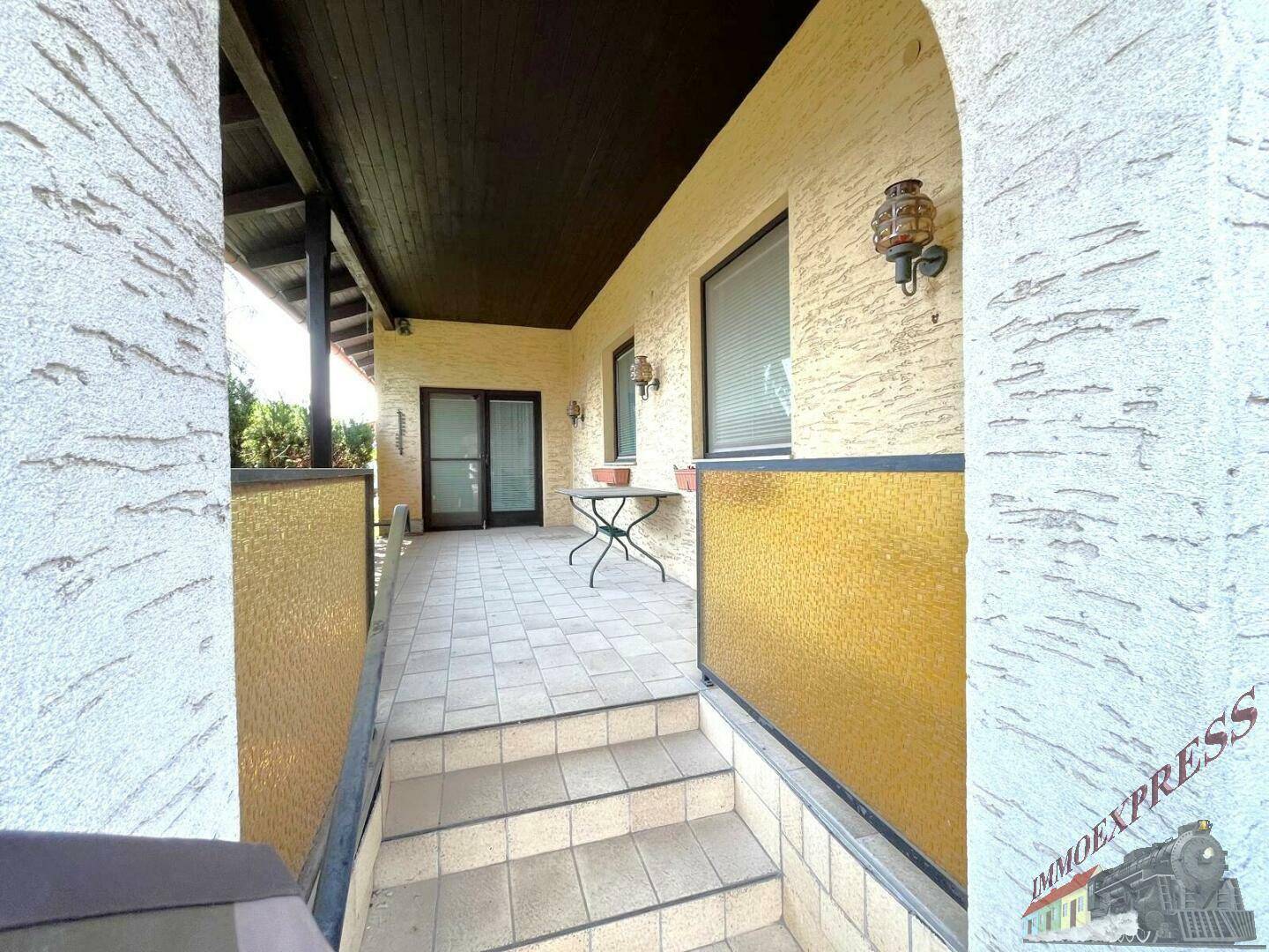 Überdachte Terrasse mit Fliesenboden und Zugang zum Innenbereich des Hauses.