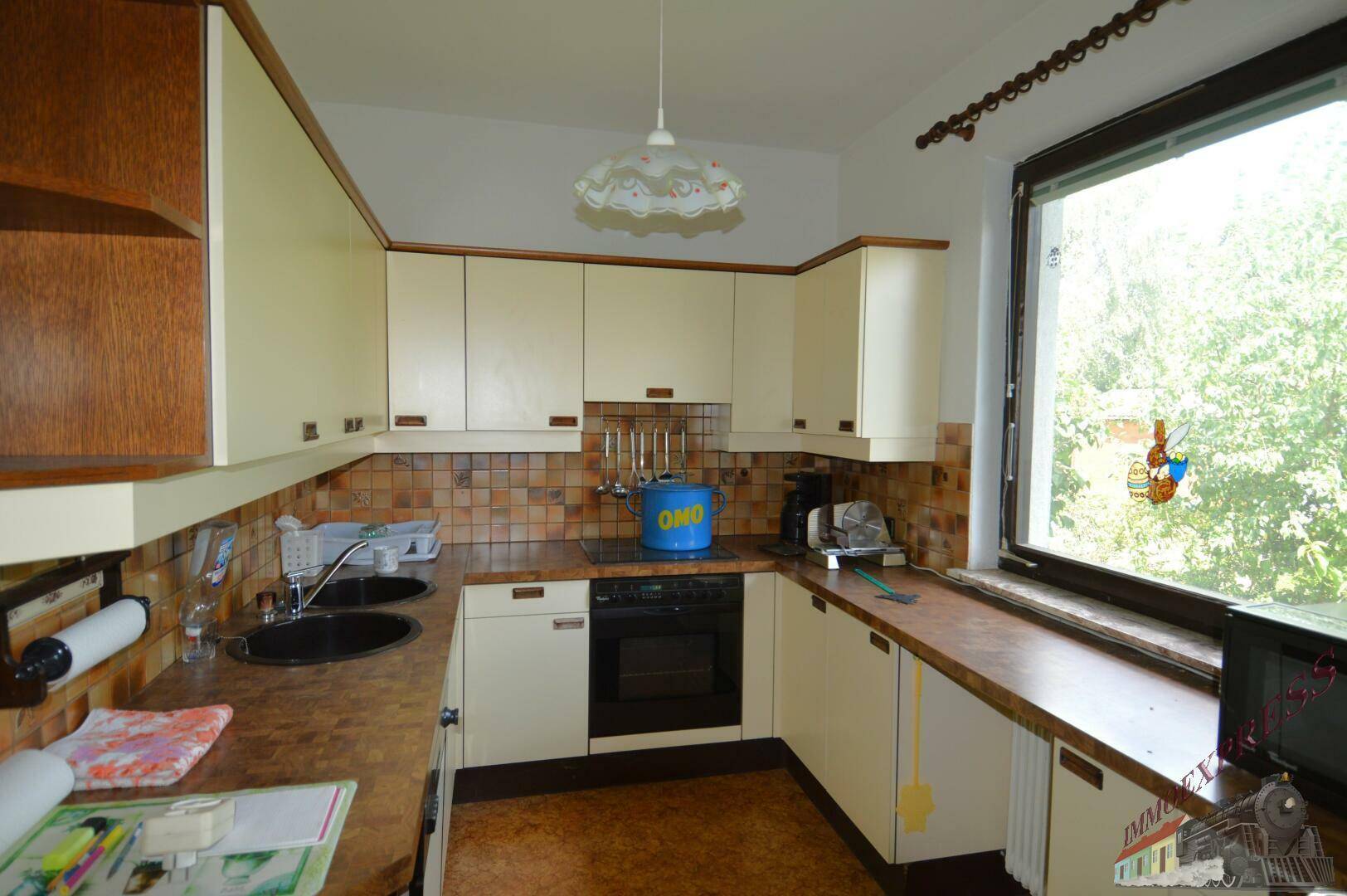 Funktionale Küche mit beigen Schränken, Fliesenrückwand und Fenster mit Gartenblick.