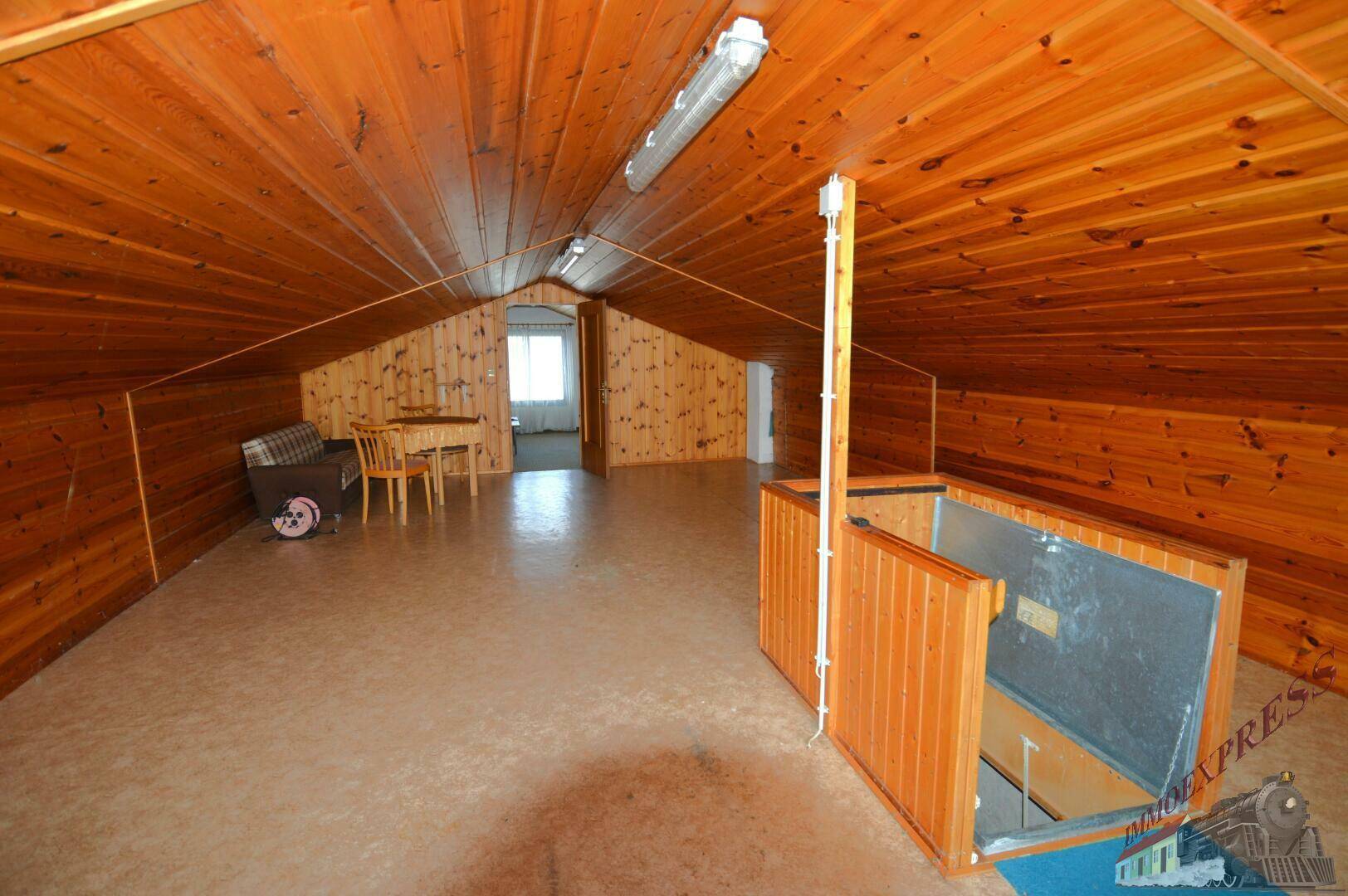 Großer Dachboden mit Holzvertäfelung, Fenster und Zugang zu weiteren Bereichen.