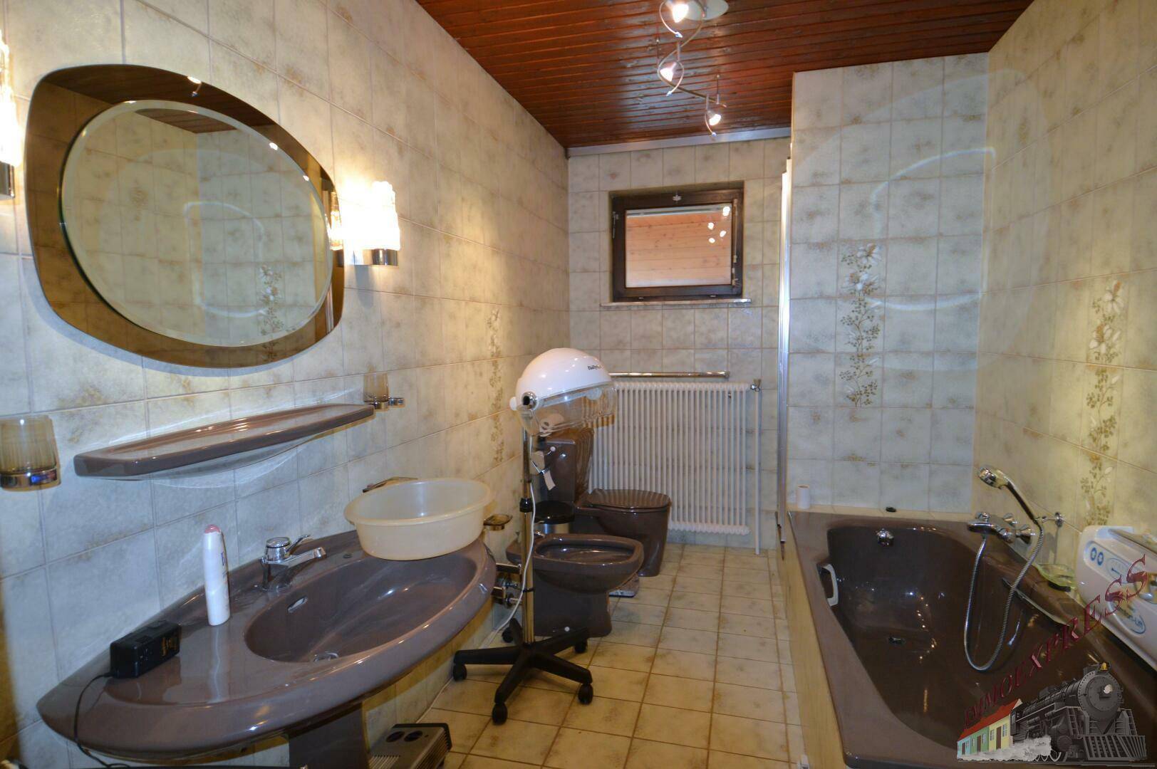 Badezimmer mit Badewanne, Waschbecken, WC, Bidet und Fenster, gefliest in beigen Tönen.