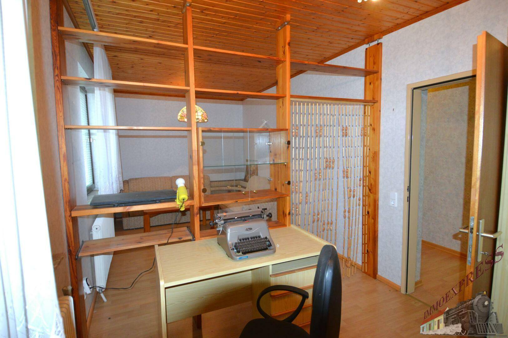 Arbeitszimmer mit Holzdecke, Regalsystem und Schreibtisch am Fenster.