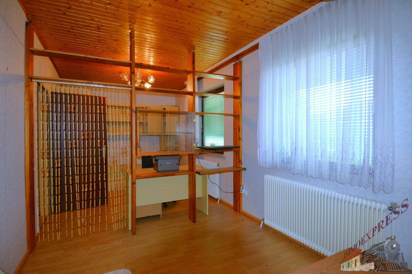 Helles Arbeitszimmer mit Holzdecke, Regalsystem und großem Fenster.