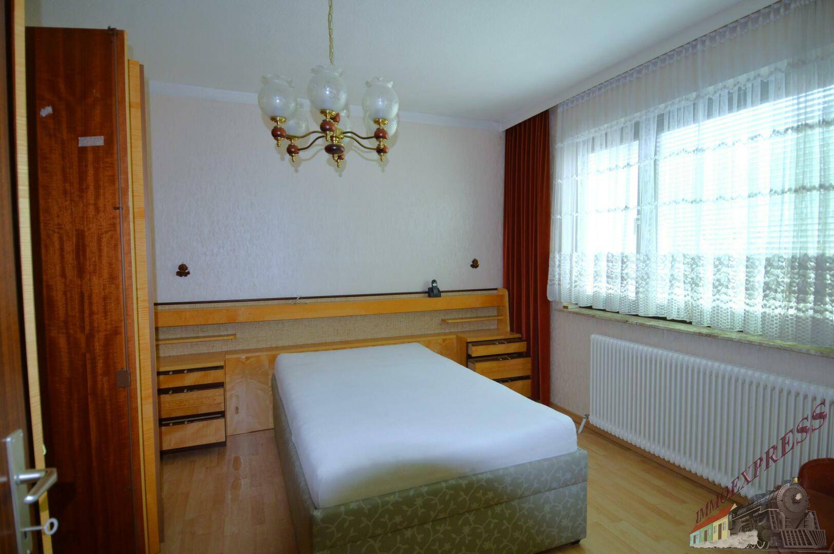 Schlafzimmer mit Doppelbett, Holzschrank und Fenster mit Vorhängen.